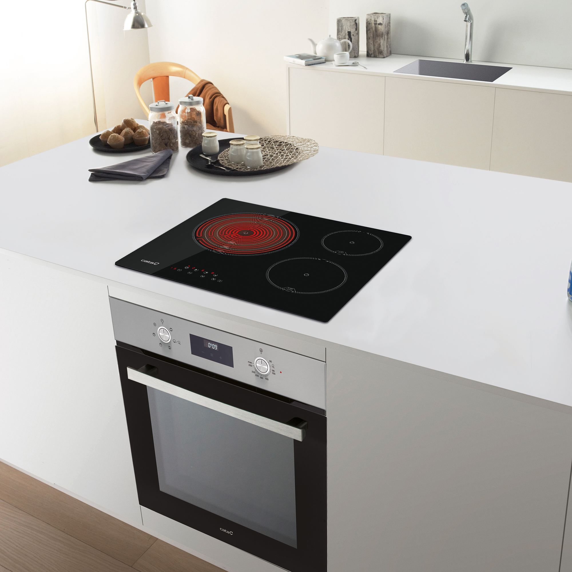 Isola cucina con piano cottura a induzione nero e forno sottostante, stanza luminosa.