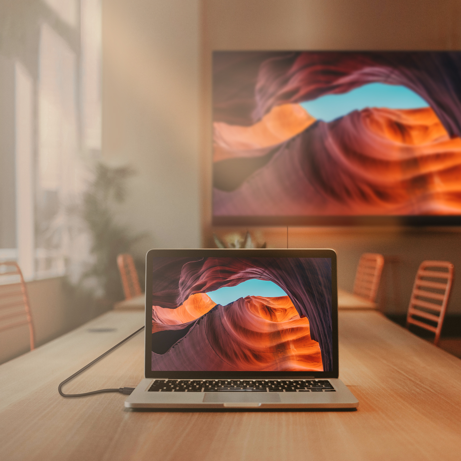Laptop op een houten tafel, verbonden met een groter scherm met een canyon-afbeelding.