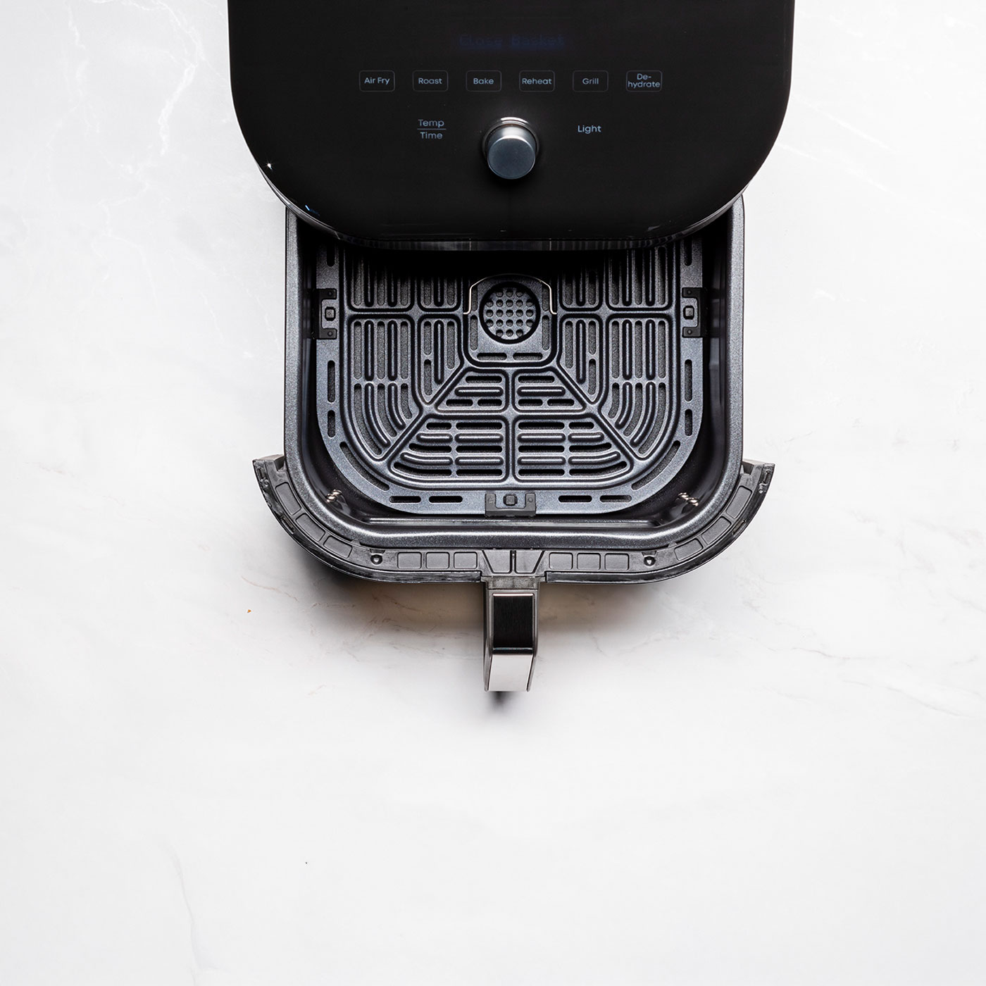 Czarna frytownica powietrzna z otwartą pokrywą, czarnym koszem w środku, na białym marmurze.