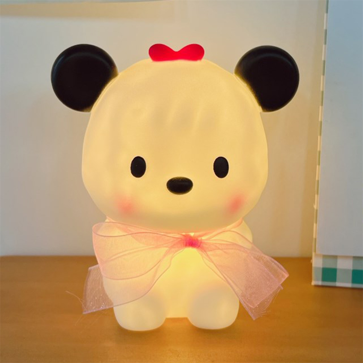 Eine niedliche, cartoonartige Bärenlampe. Die Lampe ist weiß mit schwarzen Ohren, einer roten Schleife und rosa Wangen.
