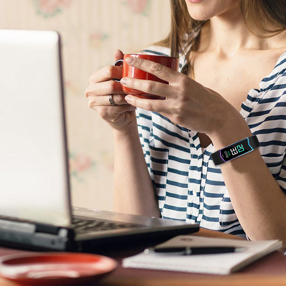 Eine Person mit Smart-Armband, arbeitet am Laptop und trinkt Kaffee. Ein Notizblock liegt daneben.