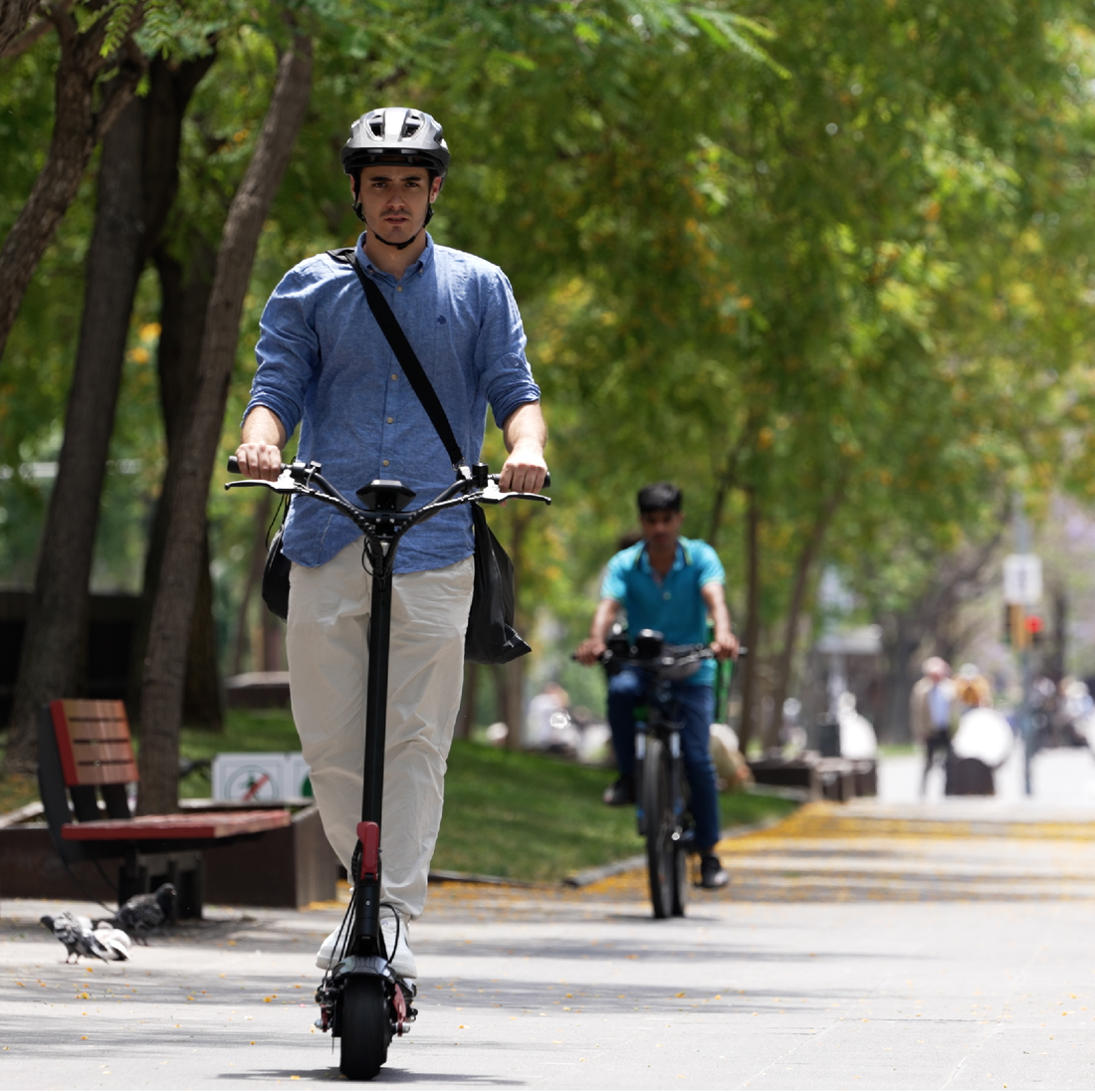 Un hombre con casco monta un patinete eléctrico en un camino, otro en bicicleta en el fondo.