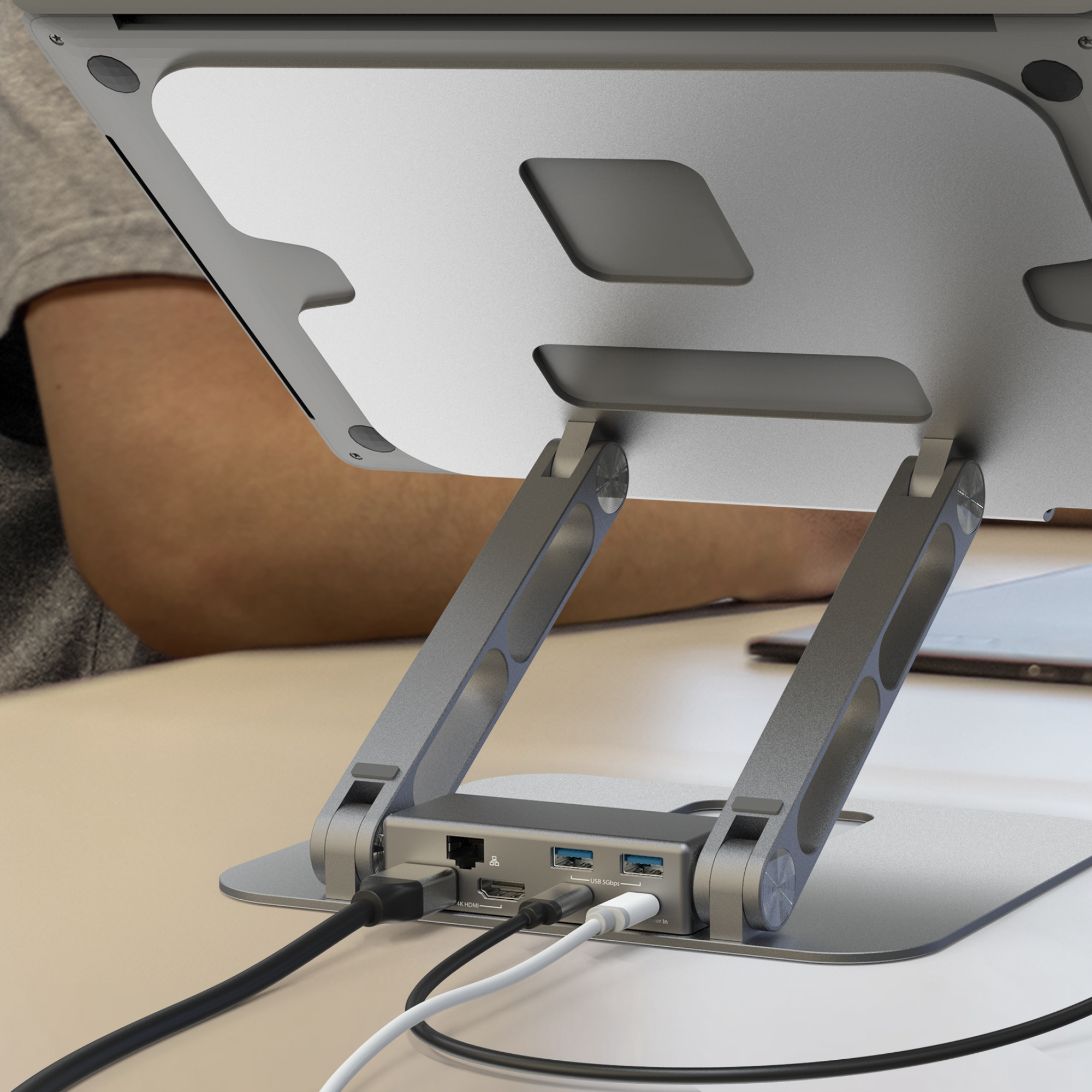 Laptop an silberne Dockingstation mit Anschlüssen angeschlossen. Arm einer Person sichtbar.