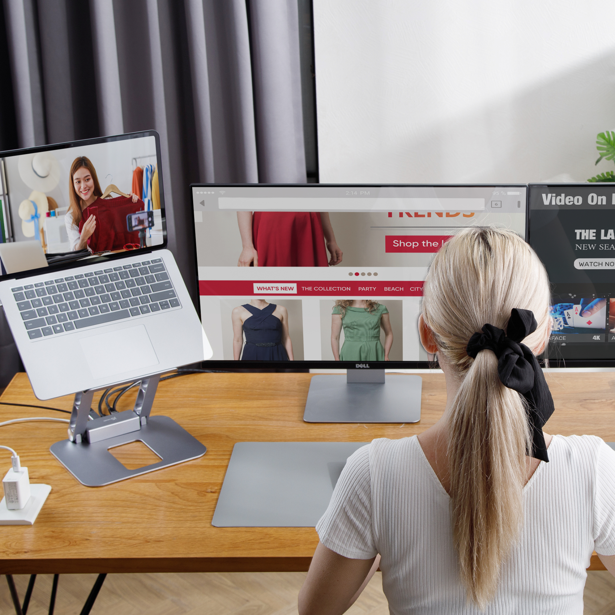 Eine Frau arbeitet an einem Schreibtisch mit Laptop und Monitor. Ein weiterer Laptop steht auf einem Ständer.