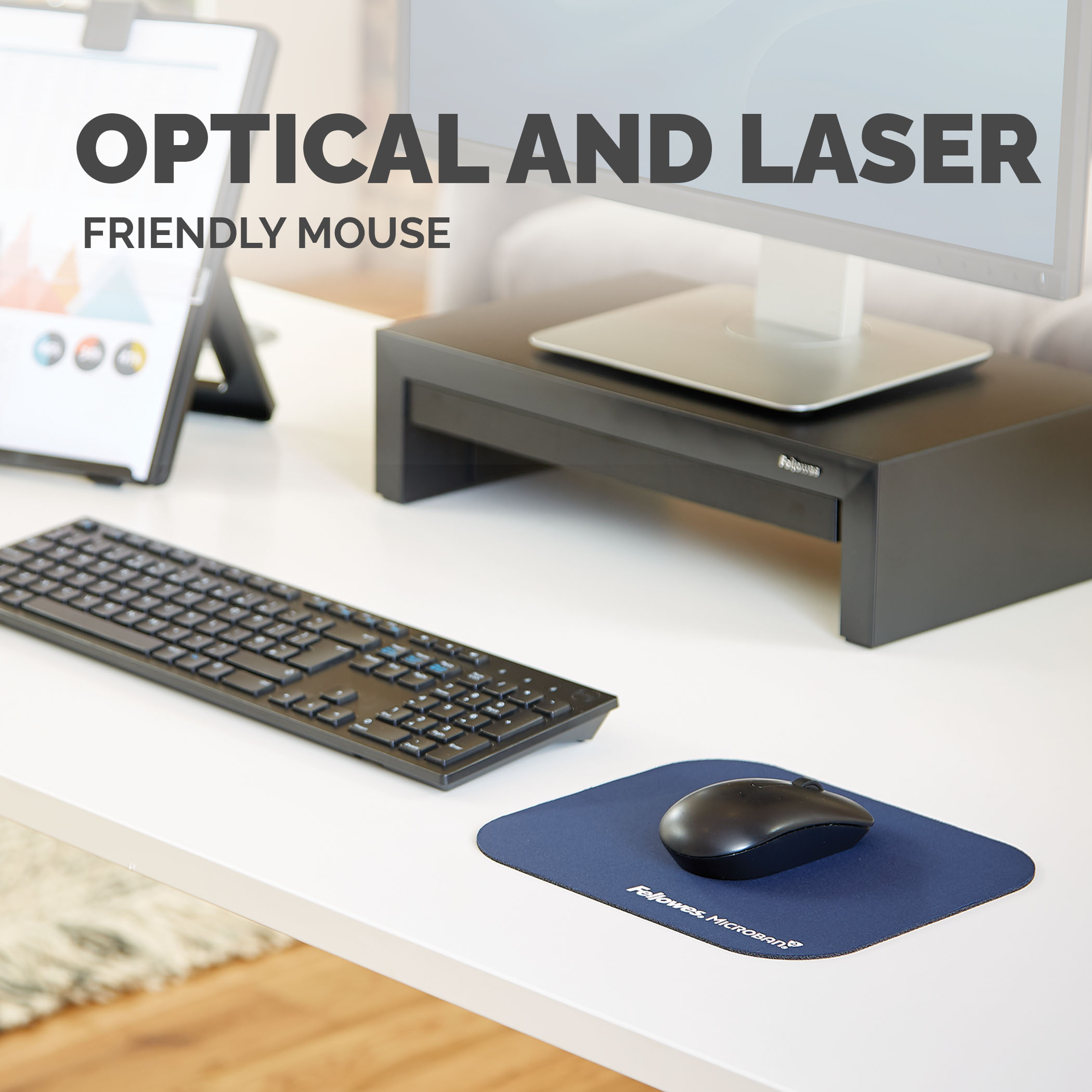 Mouse e tastiera su una scrivania bianca. Un monitor con supporto nero sullo sfondo.