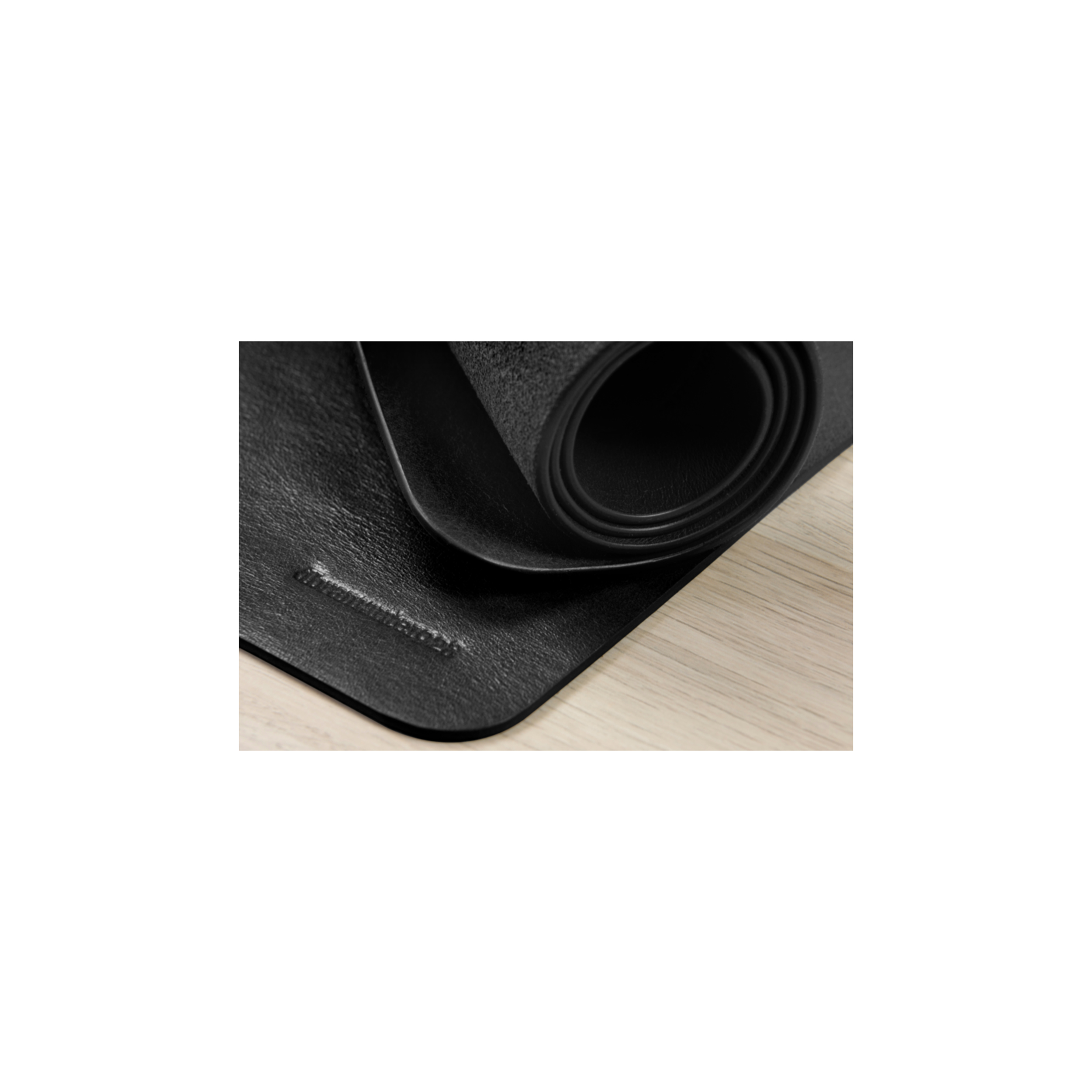 Eine aufgerollte schwarze Yogamatte auf einer hellen Holzoberfläche, die Ecke und Textur zeigt.