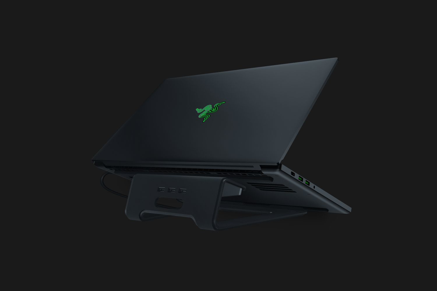 Czarny laptop na podstawce, zielone logo, widok z boku, ciemne tło.