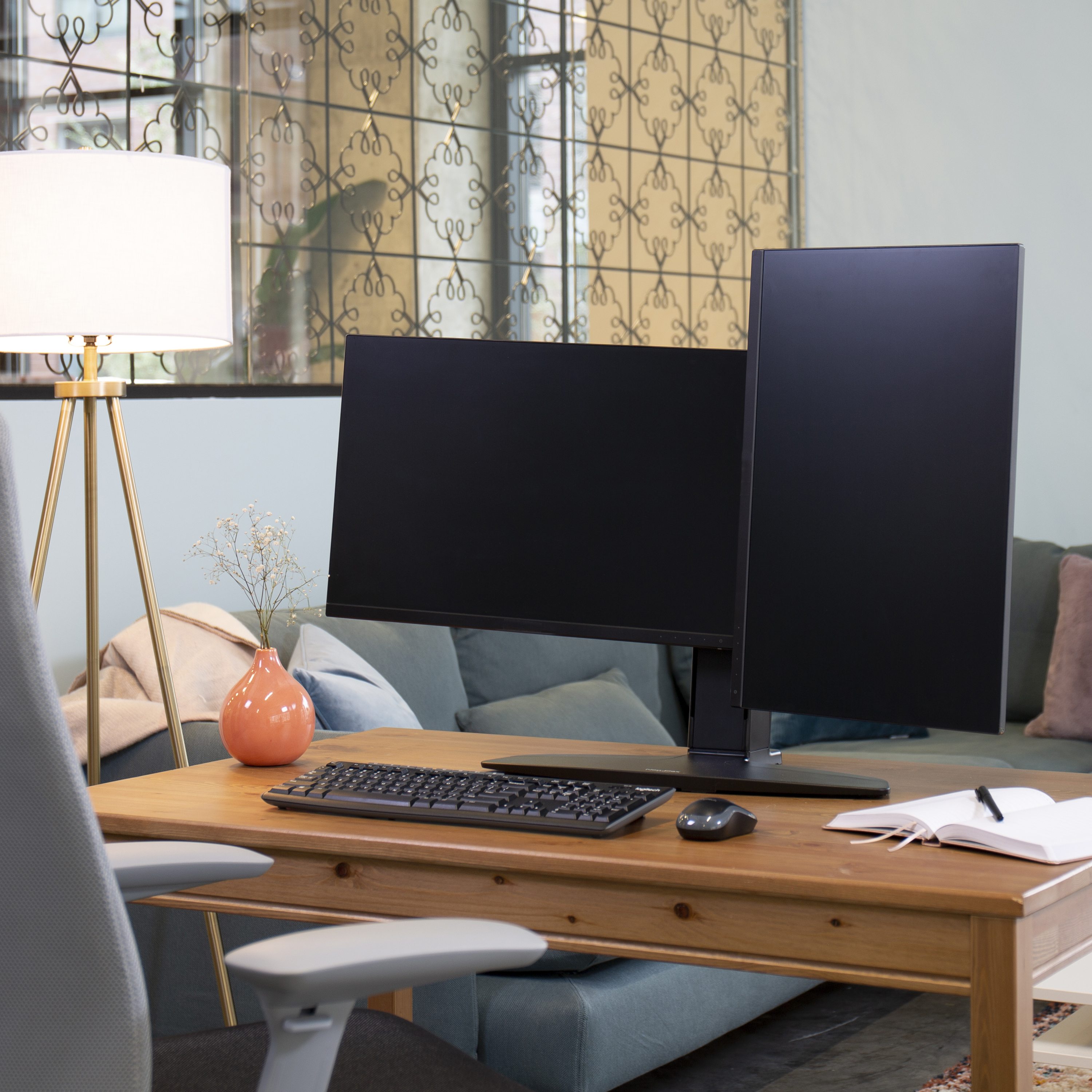 Bureau met twee monitoren, toetsenbord, muis, notitieboek en lamp.