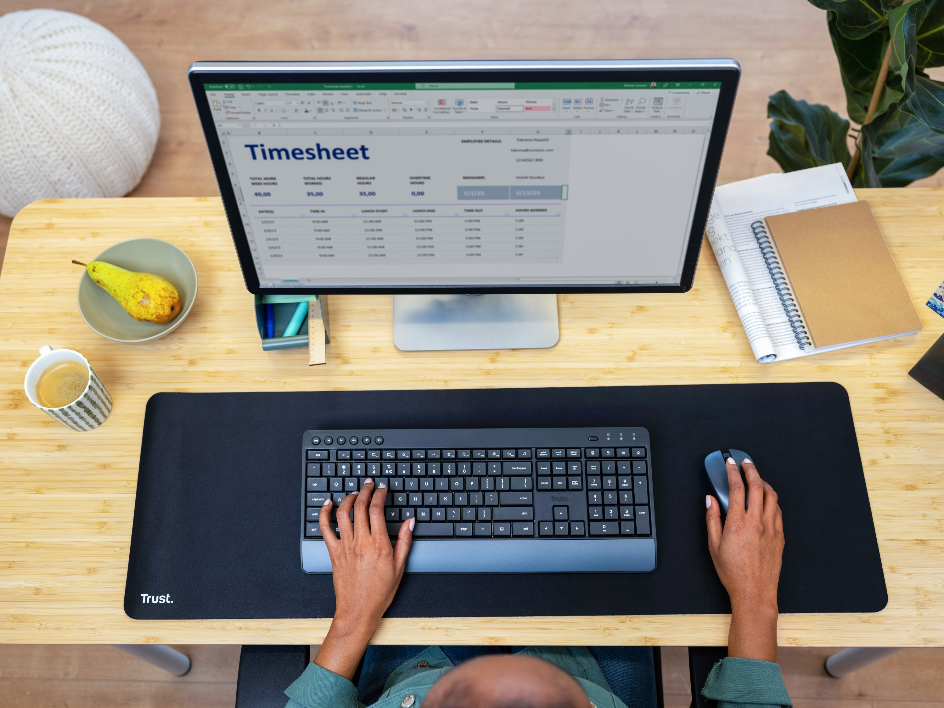 Osoba pisząca na klawiaturze z monitorem pokazującym kartę czasu pracy, gruszkę i filiżankę kawy.