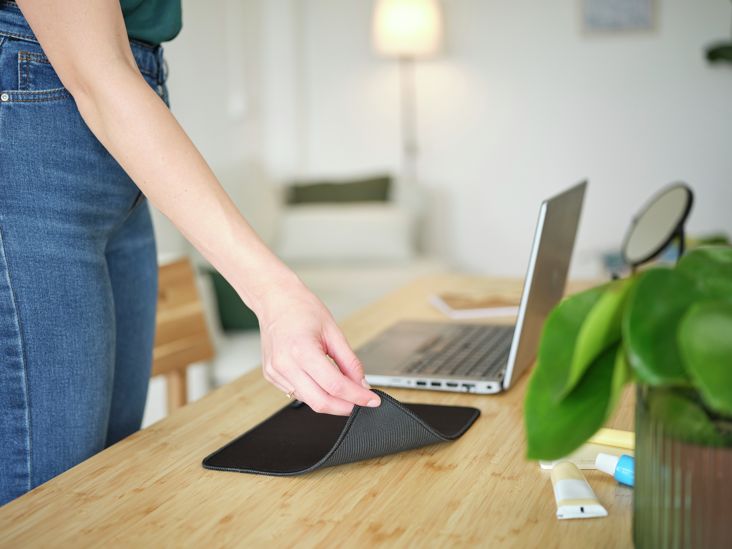 Mano che tiene un tappetino nero, accanto a un laptop e articoli da toeletta su una scrivania.