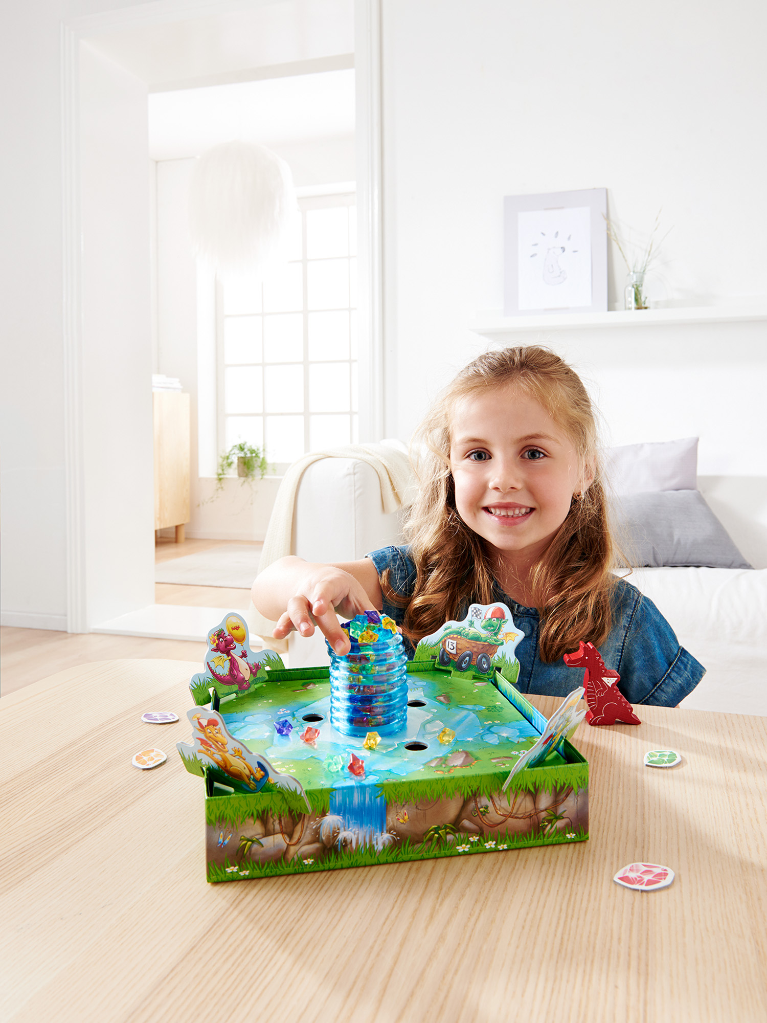 Ein lächelndes Mädchen spielt ein buntes Brettspiel mit Dinosaurierthema auf einem Holztisch.