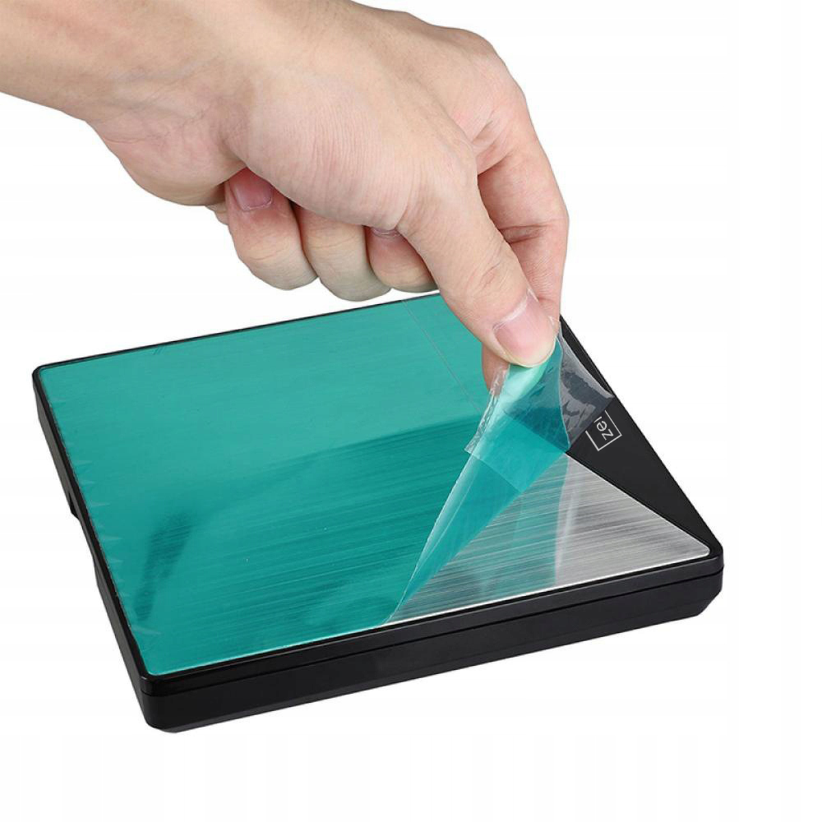 Ręka zdejmująca folię ochronną z czarnego urządzenia z zieloną powierzchnią.