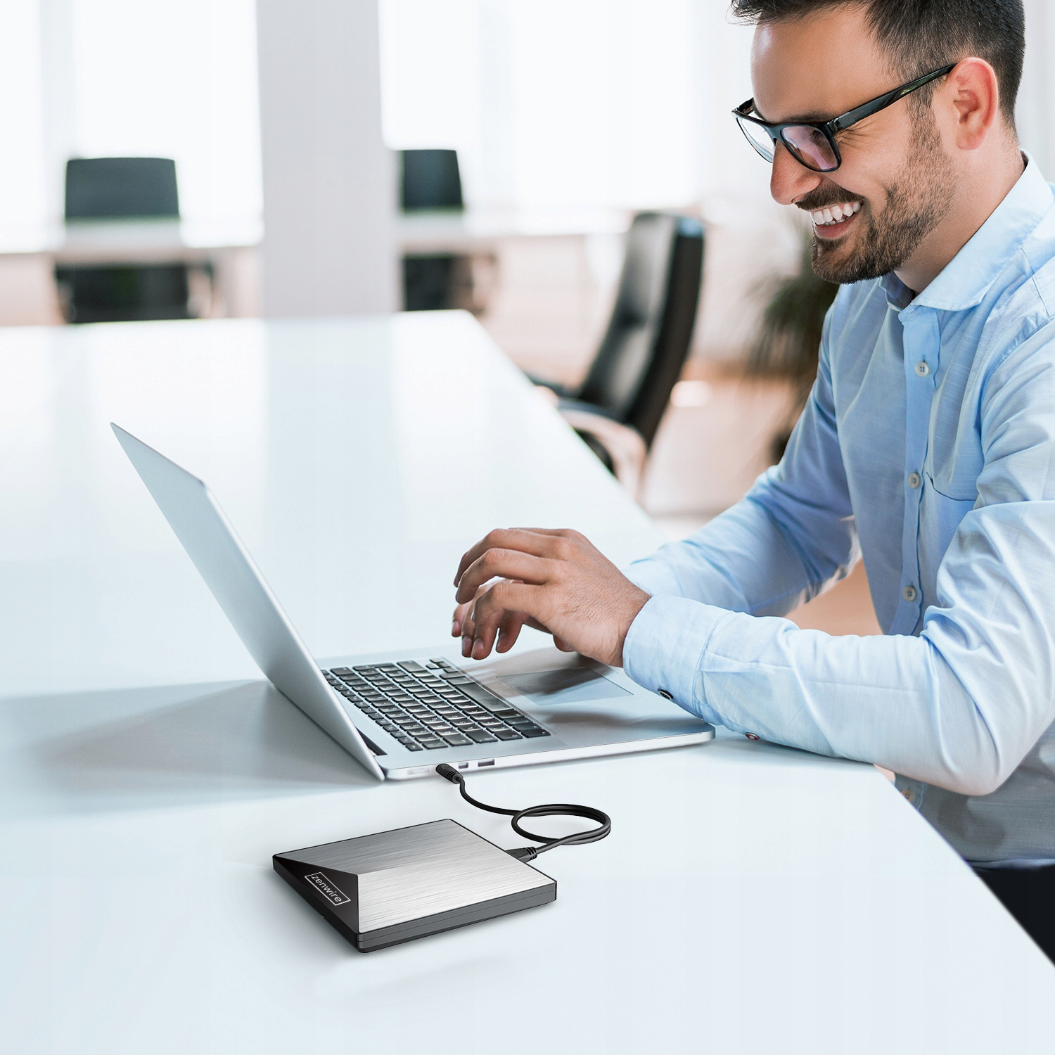 Mężczyzna pracuje na laptopie podłączonym do srebrnego zewnętrznego dysku twardego na białym biurku.