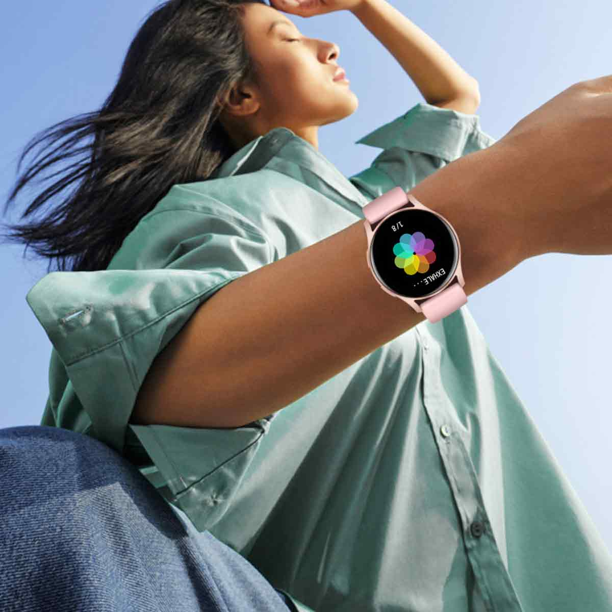 Eine Frau trägt eine Smartwatch mit buntem Blumendesign, blauer Himmel im Hintergrund.