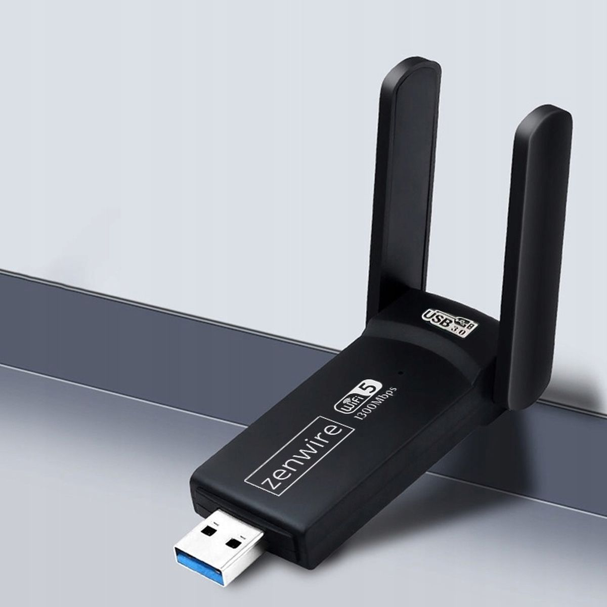 Czarny adapter WiFi USB z dwiema antenami. Jest podłączony do portu USB na szarej powierzchni.
