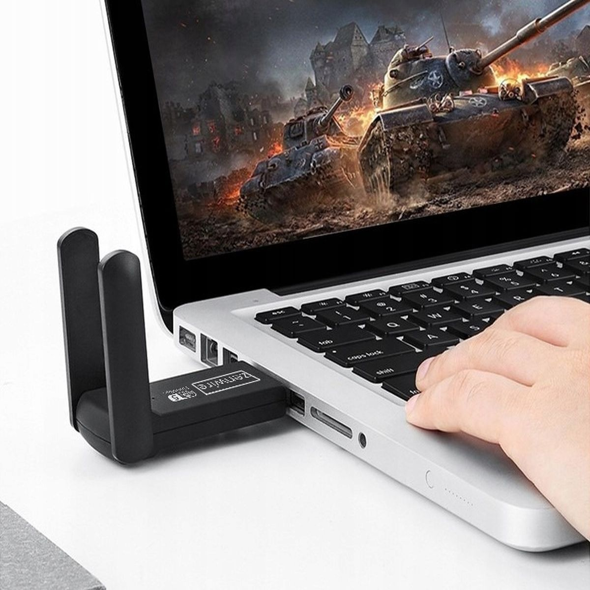 Adapter WiFi USB podłączony do laptopa. Na ekranie wyświetlana jest scena z gry.