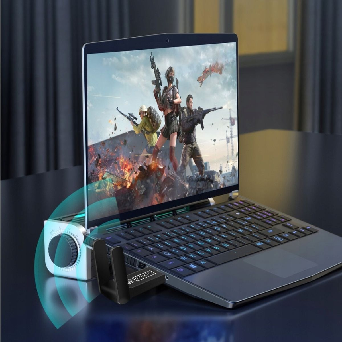 Laptop wyświetlający grę z postaciami z bronią. Widoczny głośnik bezprzewodowy i klawiatura.