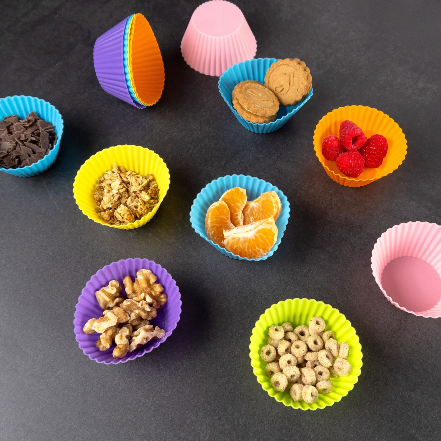 Bunte Cupcake-Förmchen gefüllt mit Lebensmitteln: Keksen, Obst, Nüssen und Schokolade. Dunkler Hintergrund.