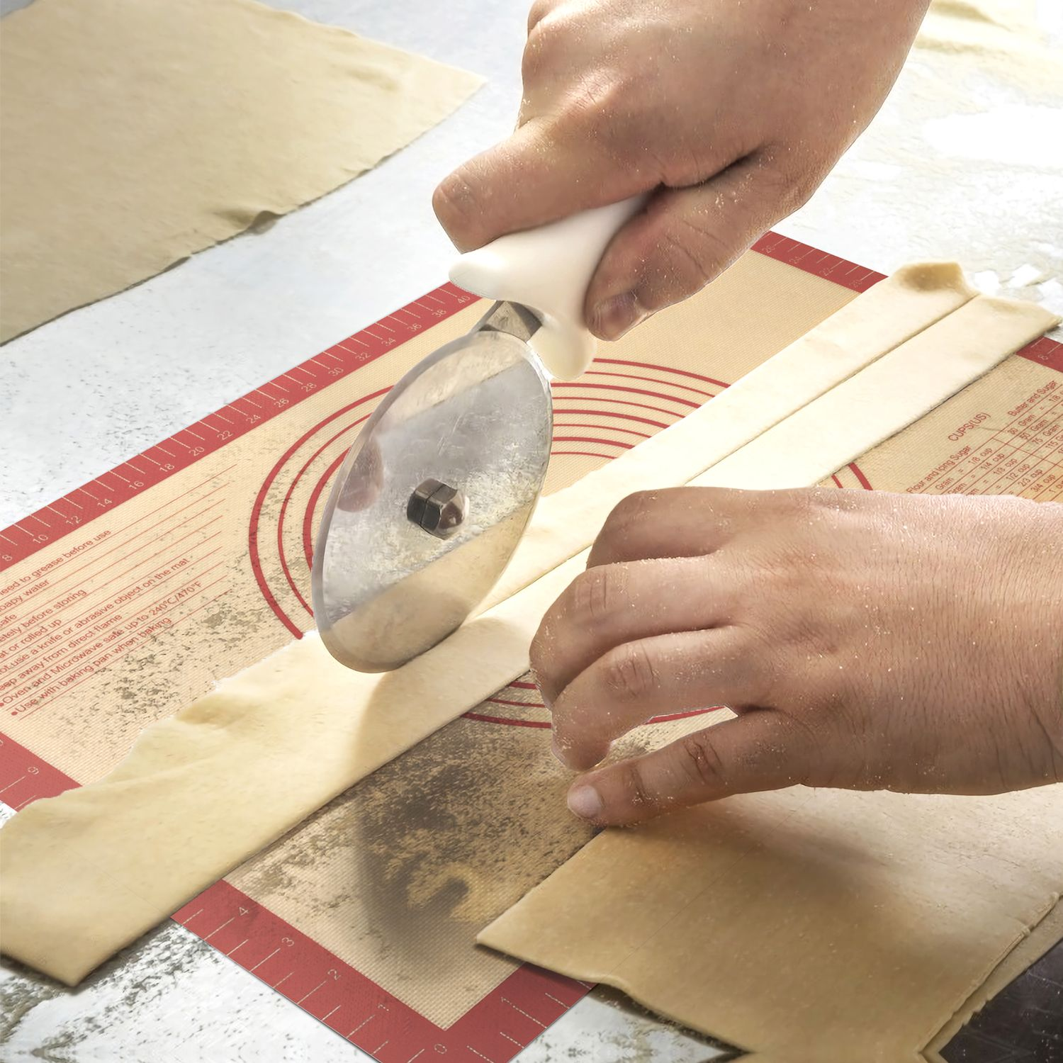 Hände schneiden mit einem Roller Teig auf roter Matte, geschnittene Teigstücke.