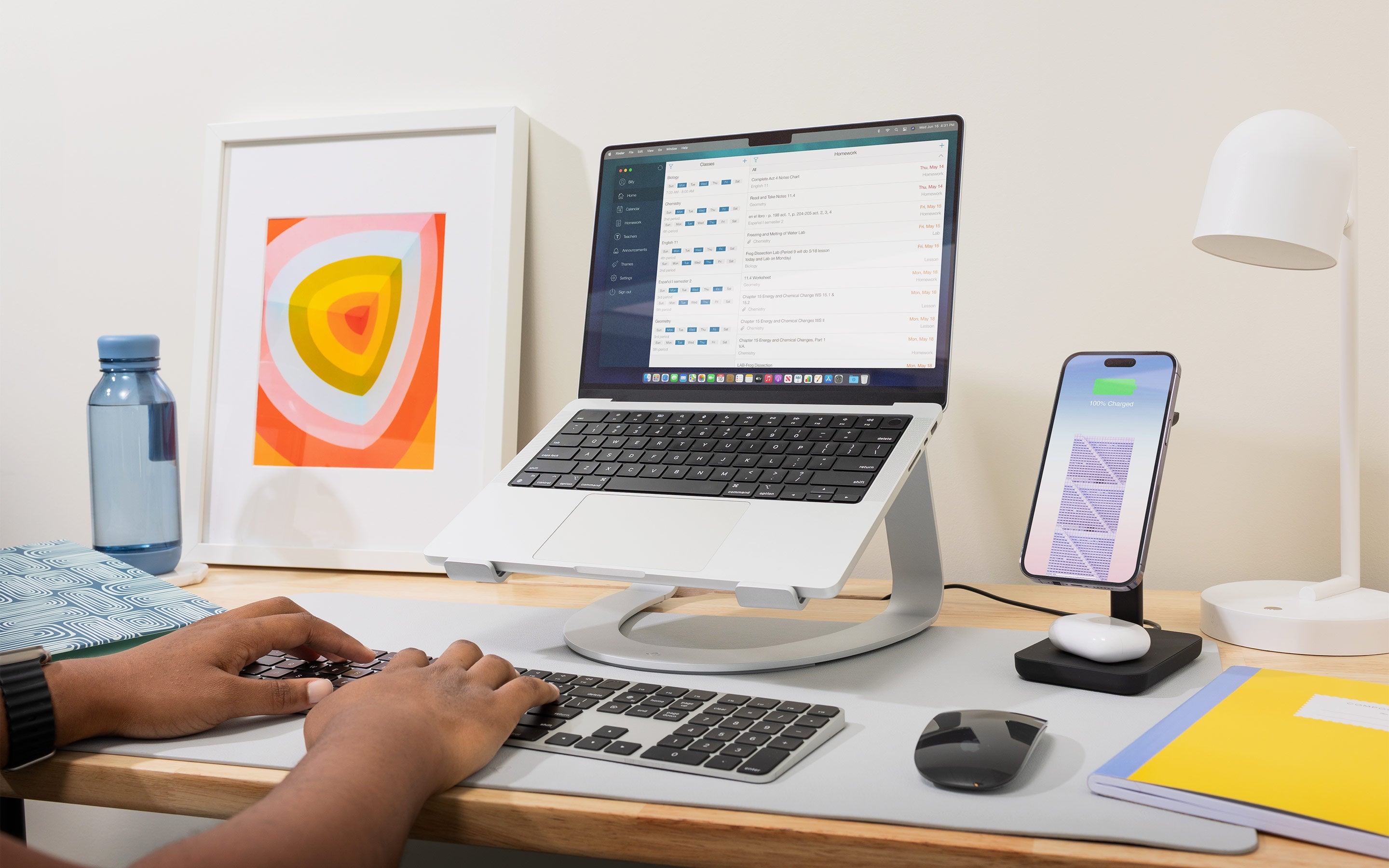 Scrivania con laptop su supporto, telefono su supporto e bottiglia d'acqua. Persona che usa la tastiera. Scrivania grigia.