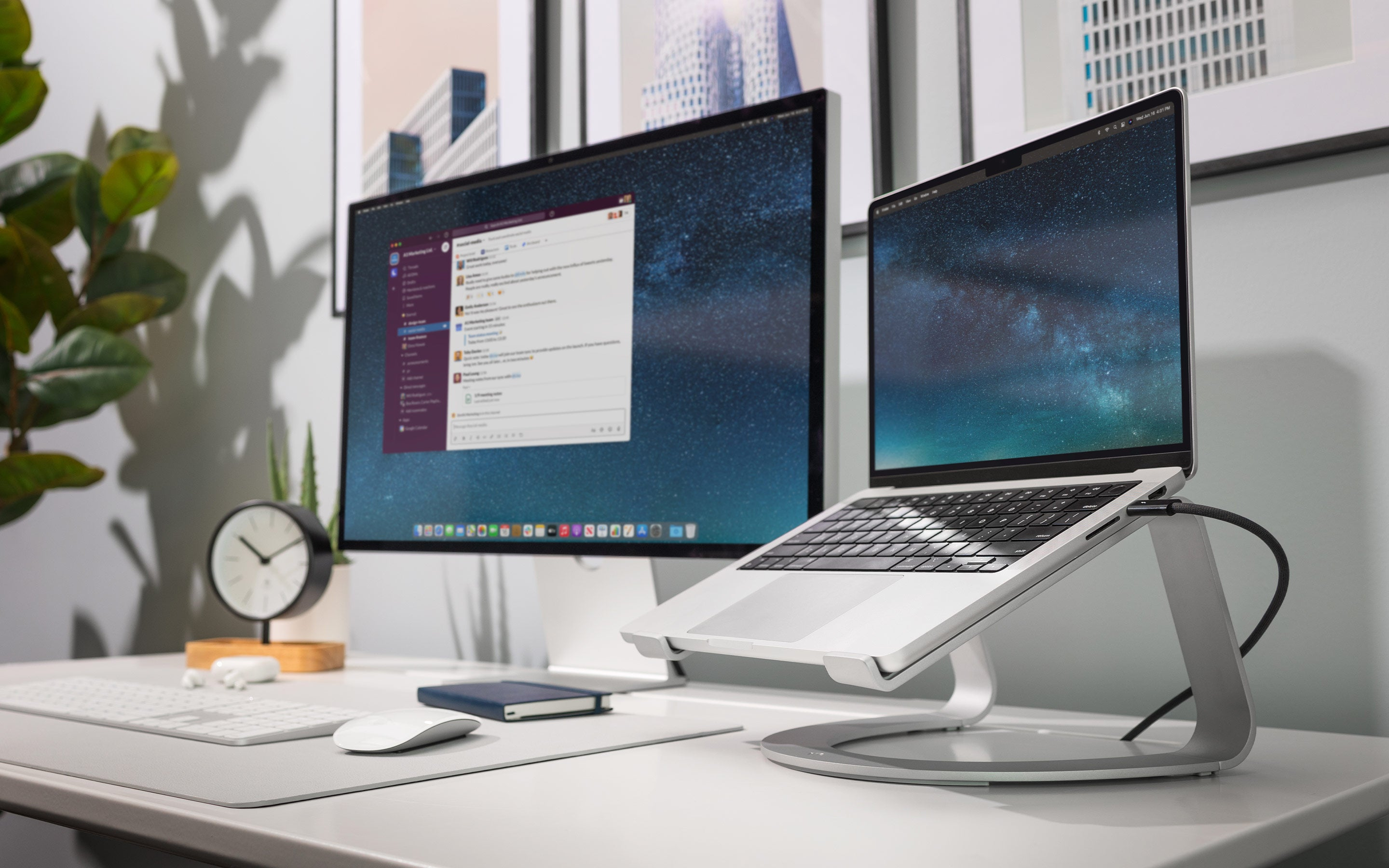 Laptop su supporto, monitor, tastiera, mouse, cuffie e decorazioni su scrivania bianca.