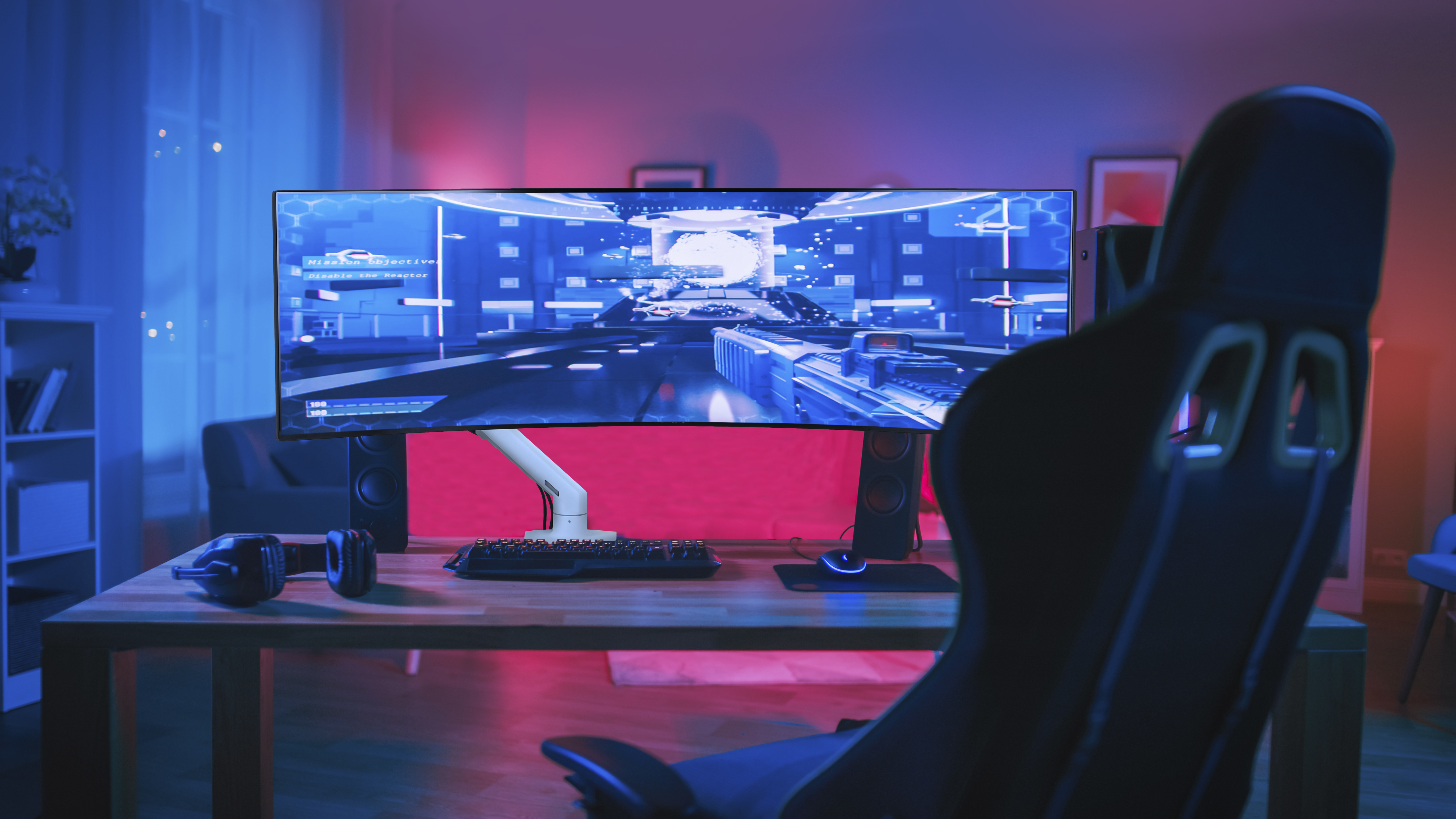 Konfiguracja pokoju do gier z monitorem, krzesłem, biurkiem i sprzętem oświetlonym niebieskimi i czerwonymi światłami.