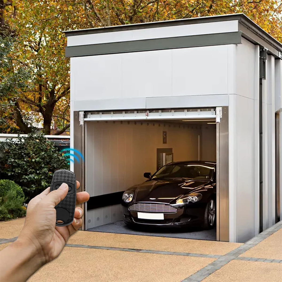 Autolift mit schwarzem Auto, Fernbedienung in der Hand. Hintergrund: Gebäude, Bäume und Himmel.