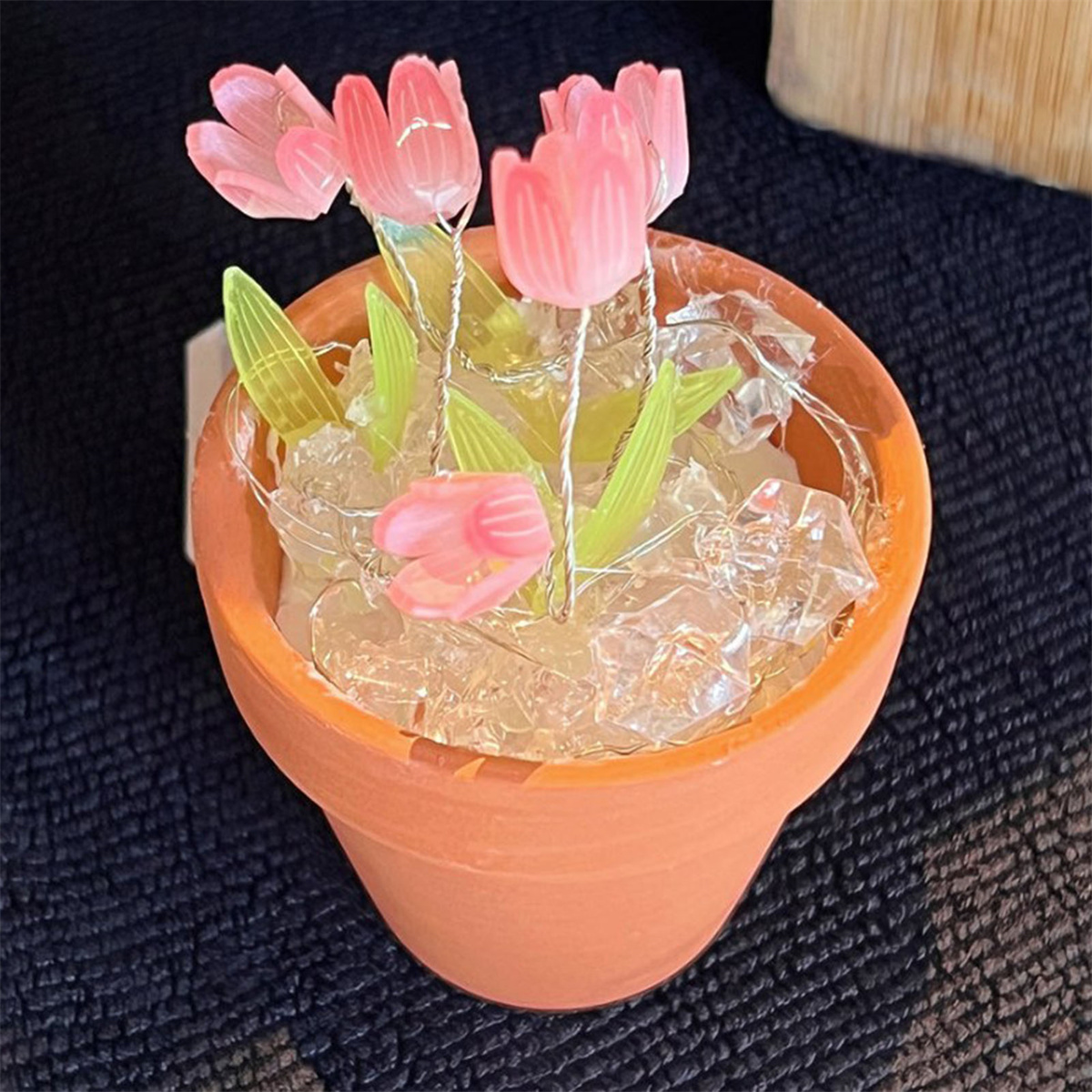 Ein kleiner Terrakotta-Topf mit rosa künstlichen Tulpen und weißen Ziersteinen.