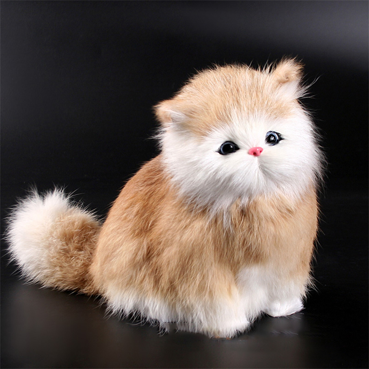 Eine flauschige Stoffkatze mit braun-weißem Fell sitzt vor schwarzem Hintergrund.