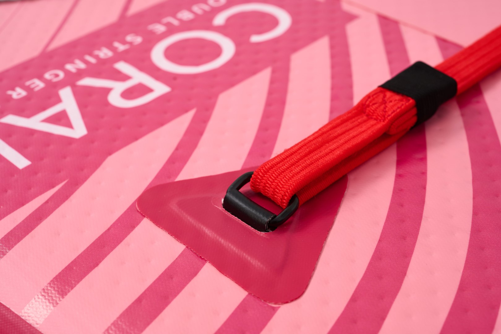Detail eines rosa-weißen Paddleboards. Roter Riemen und schwarze Schnalle. Rosa-weißes Streifendesign.