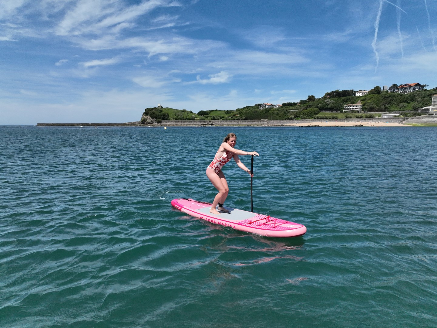 Frau paddelt an einem sonnigen Tag mit blauem Himmel auf einem rosa Brett im Meer.