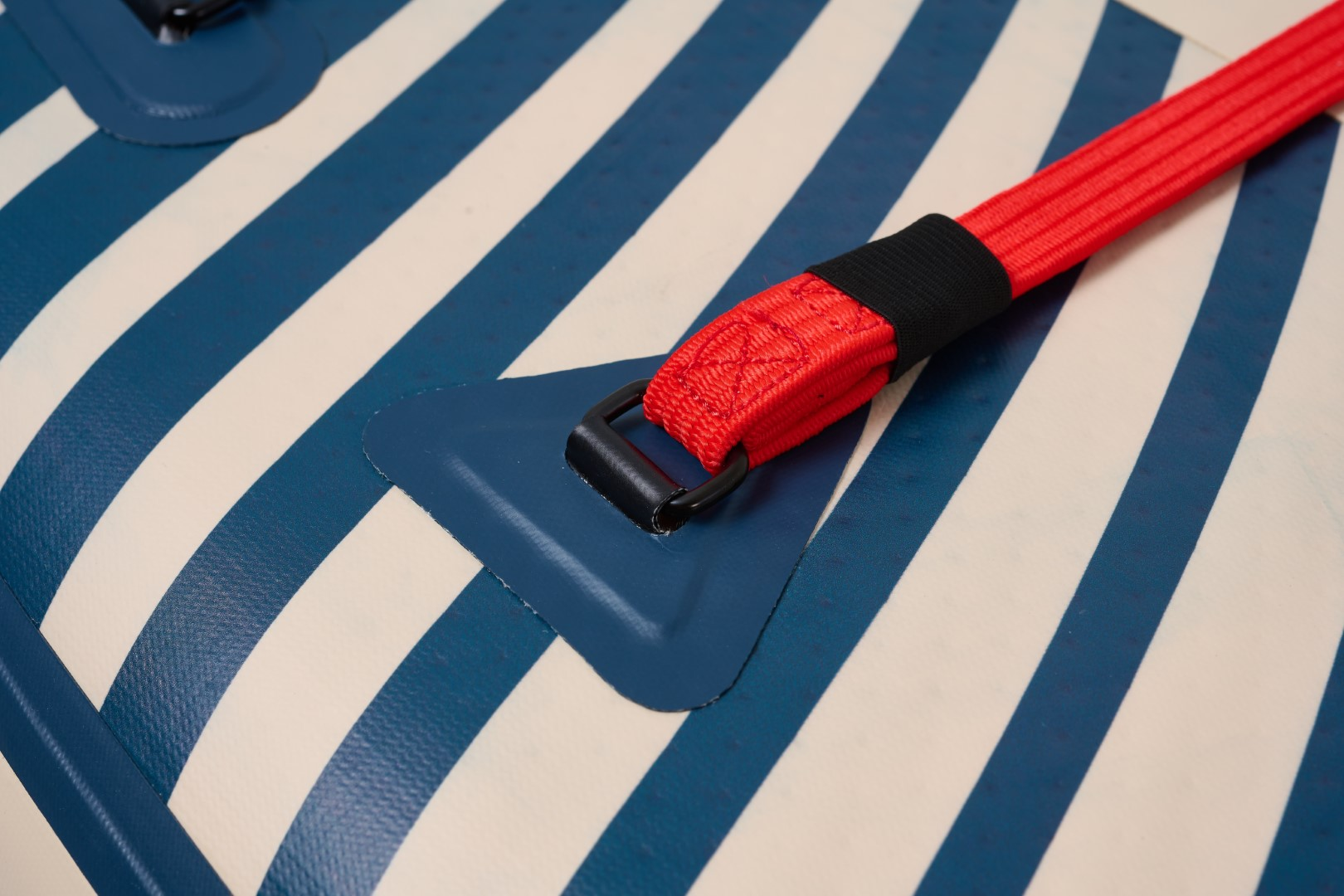 Zbliżenie deski do wiosłowania z niebiesko-białymi paskami i czerwonym paskiem z czarną klamrą.