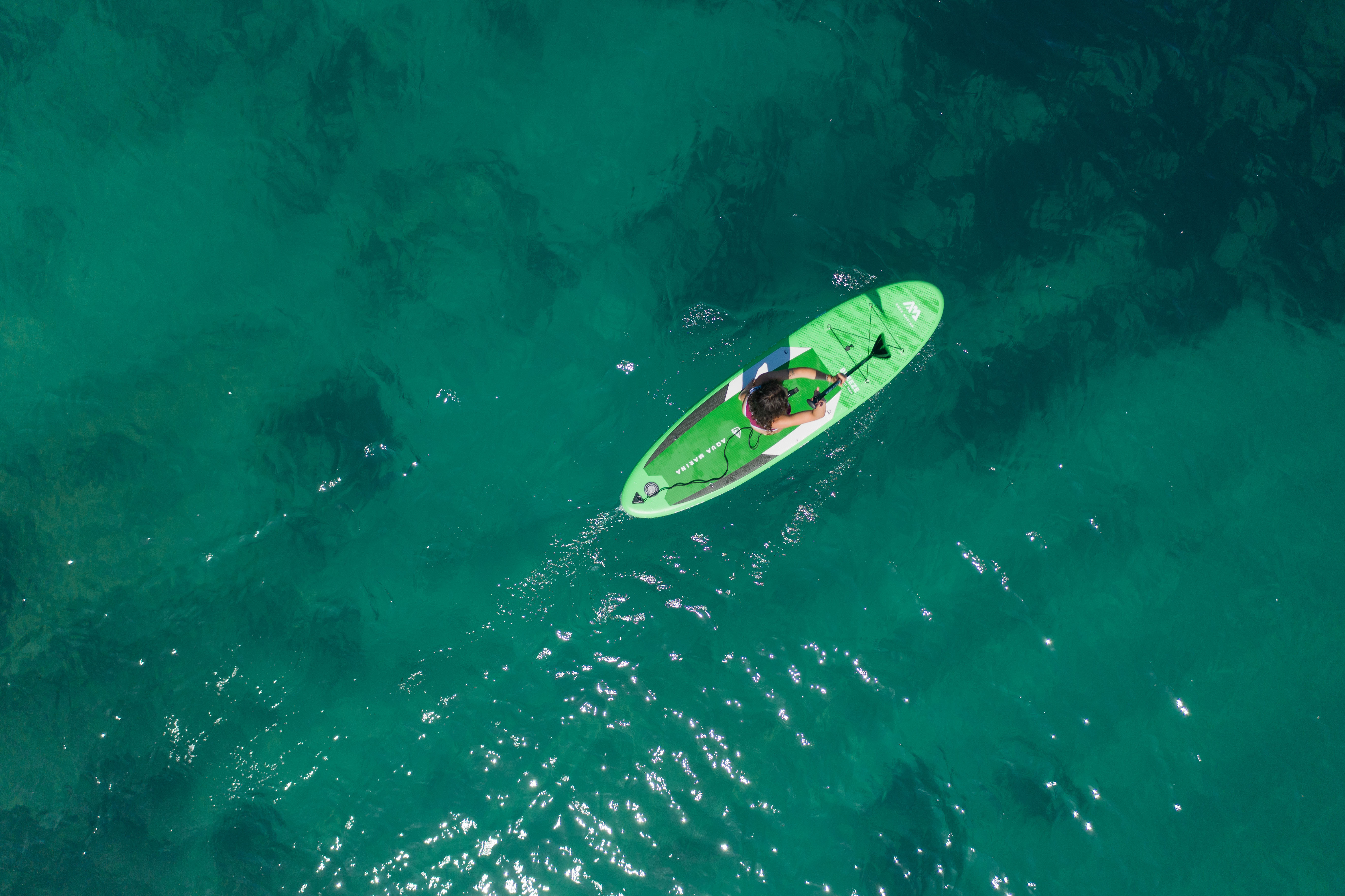 Draufsicht einer Person auf einem grünen Paddleboard in türkisblauem Wasser. Klarer, sonniger Tag.