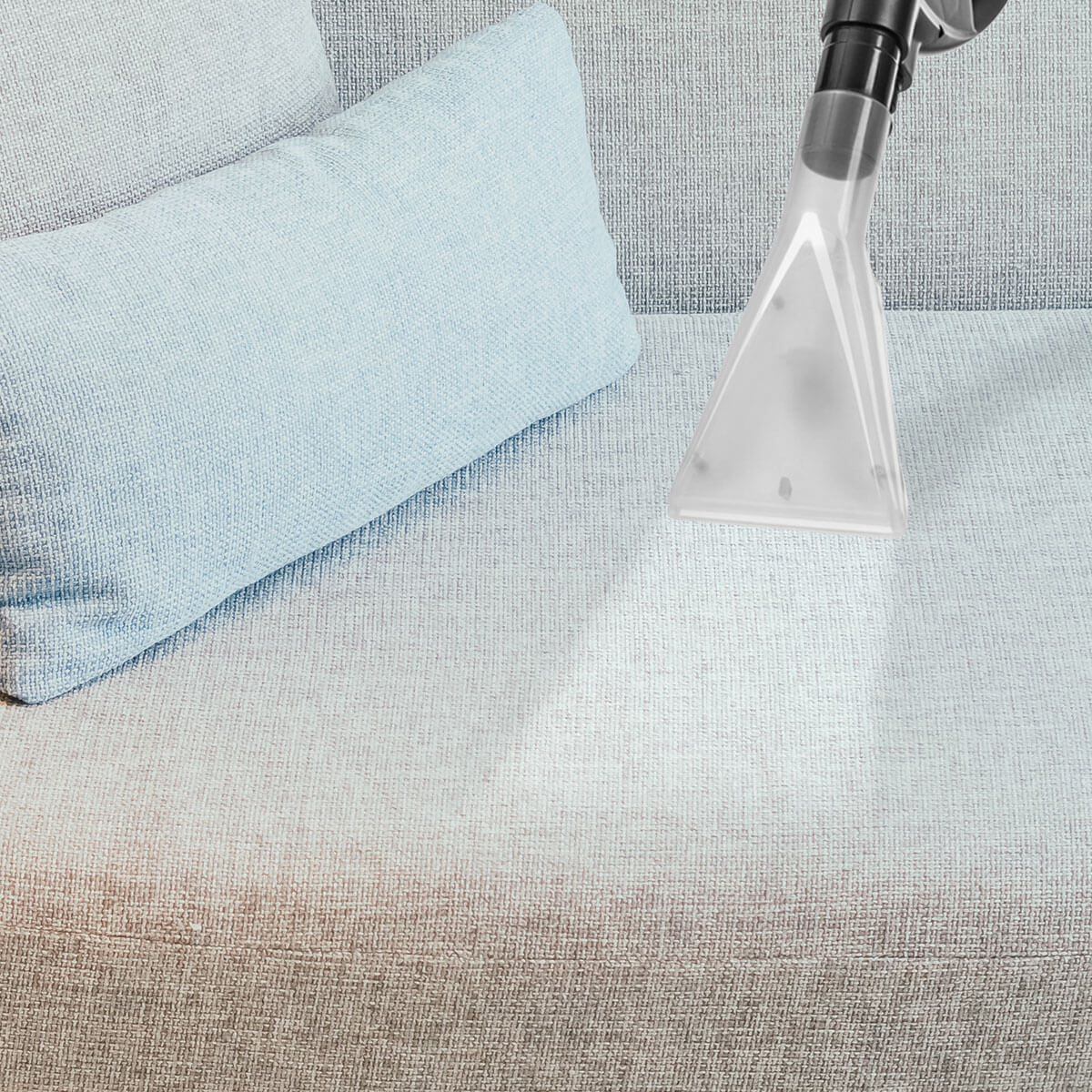 Głowica odkurzacza czyści jasnoniebieską sofę. Po lewej stronie głowicy znajduje się jasnoniebieska poduszka.