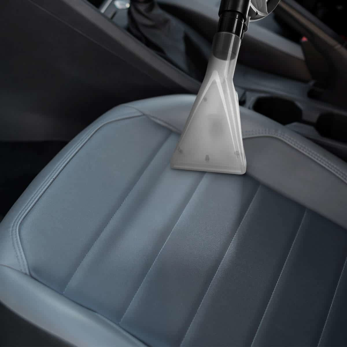 Głowica odkurzacza czyszcząca szary fotel samochodowy.