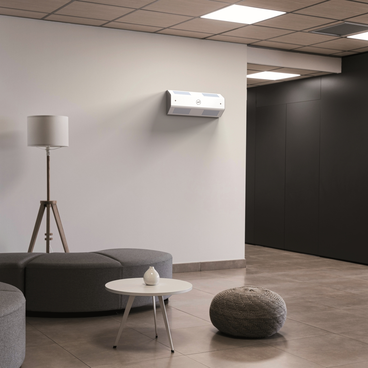 Un purificatore d'aria montato su una parete bianca in un interno moderno. Una lampada e mobili sono nella scena.