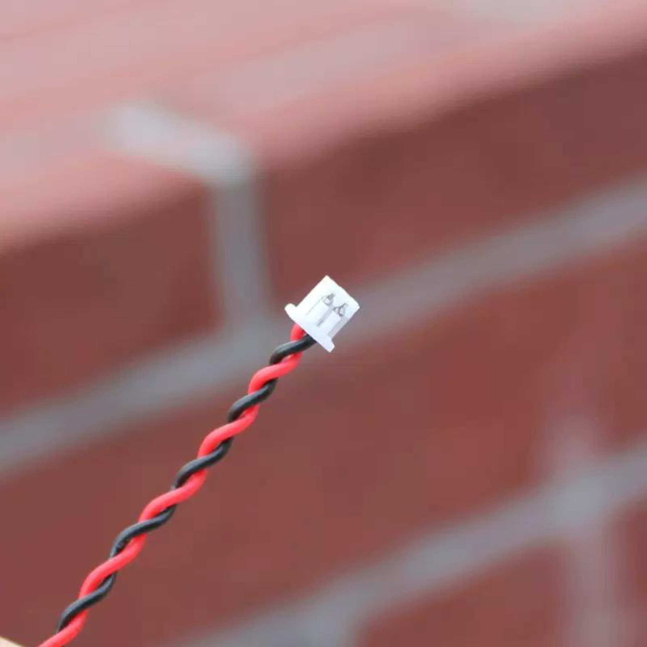Nahaufnahme von rot-schwarz verdrillten Drähten mit einem kleinen weißen Stecker am Ende.