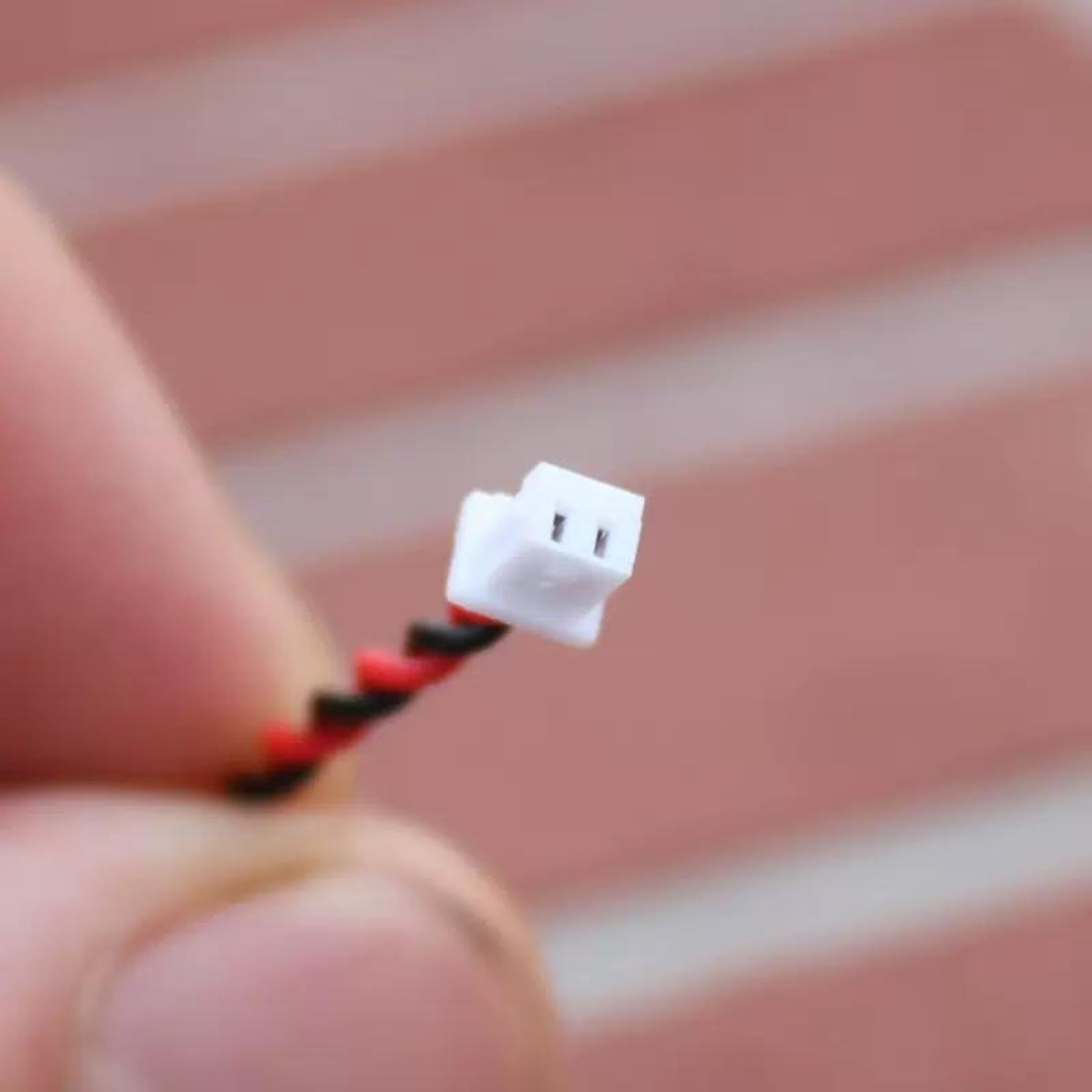 Ein kleiner weißer Stecker mit zwei Pins, verbunden mit schwarzen und roten Drähten.