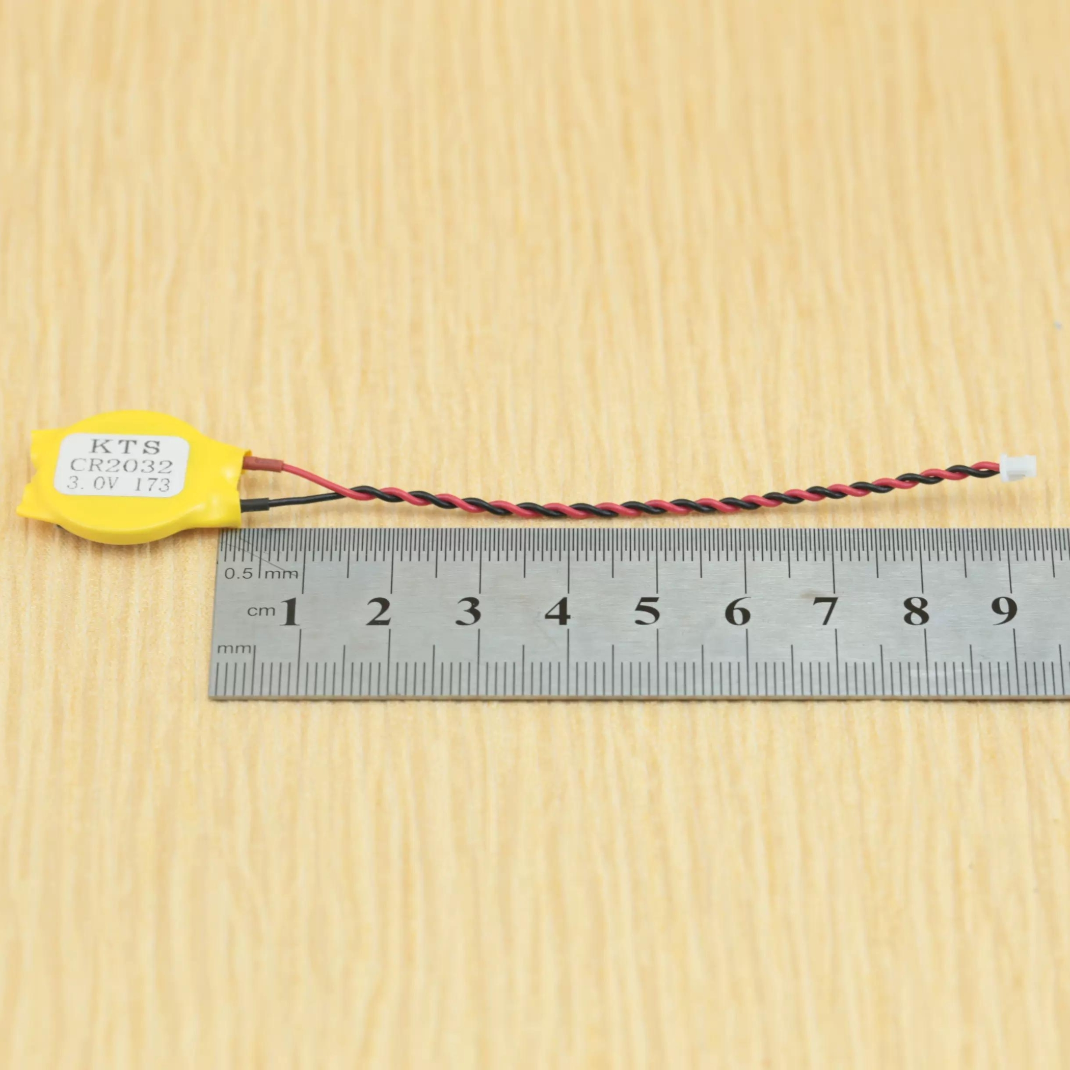 Gelbe Batterie mit zwei Drähten, neben einem Lineal. Auf der Batterie steht KTS CR2032 3.0V 173.