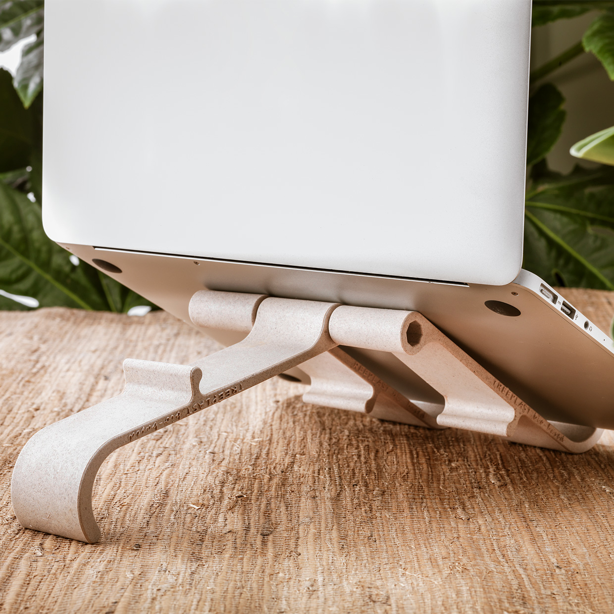 Laptop on a stand made of light-colored material. Stand has a unique design with curved supports.