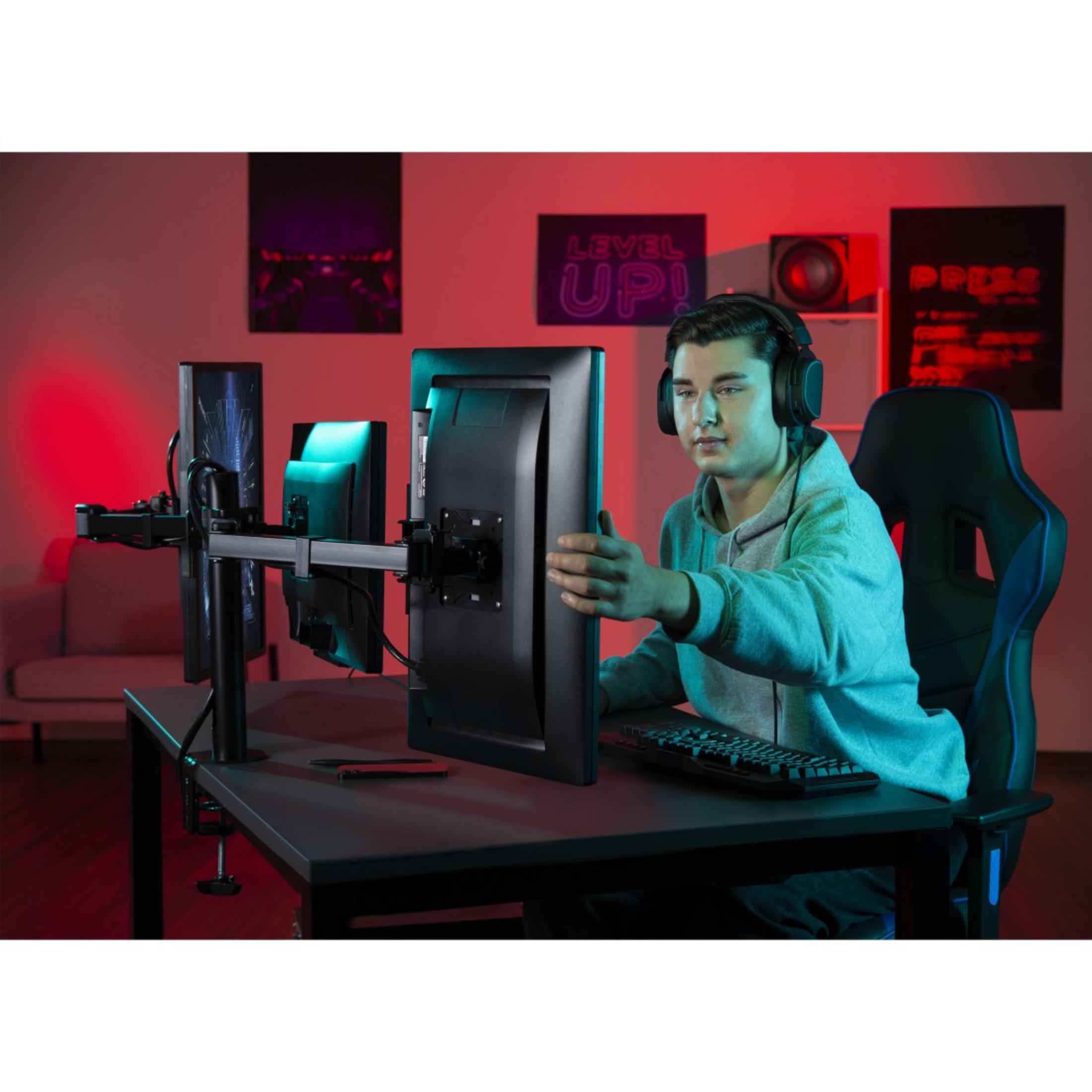 Gracz w słuchawkach przed monitorem. Na biurku klawiatura i dwa inne monitory.