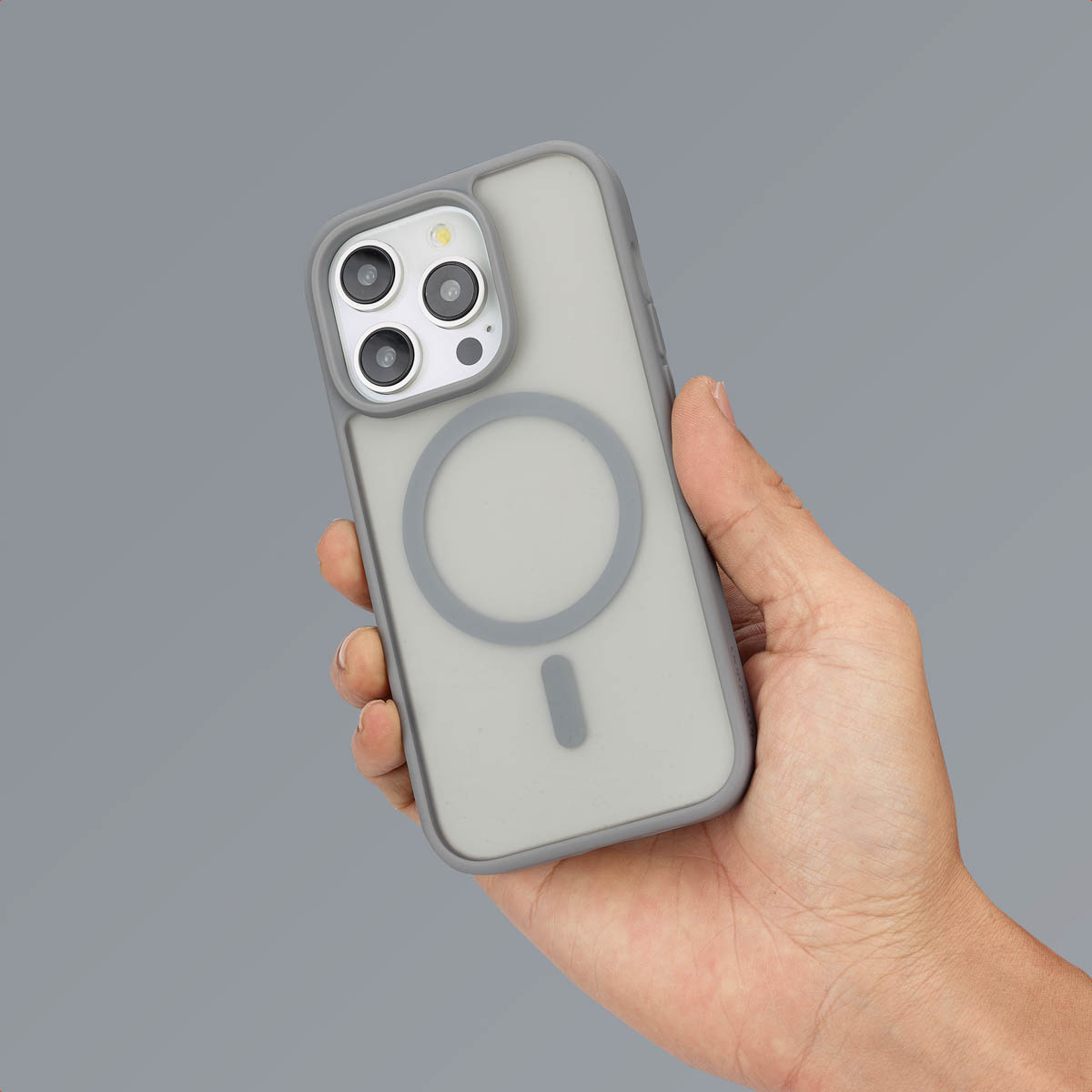 Une main tenant une coque de téléphone grise avec un cercle au milieu. Fond gris.