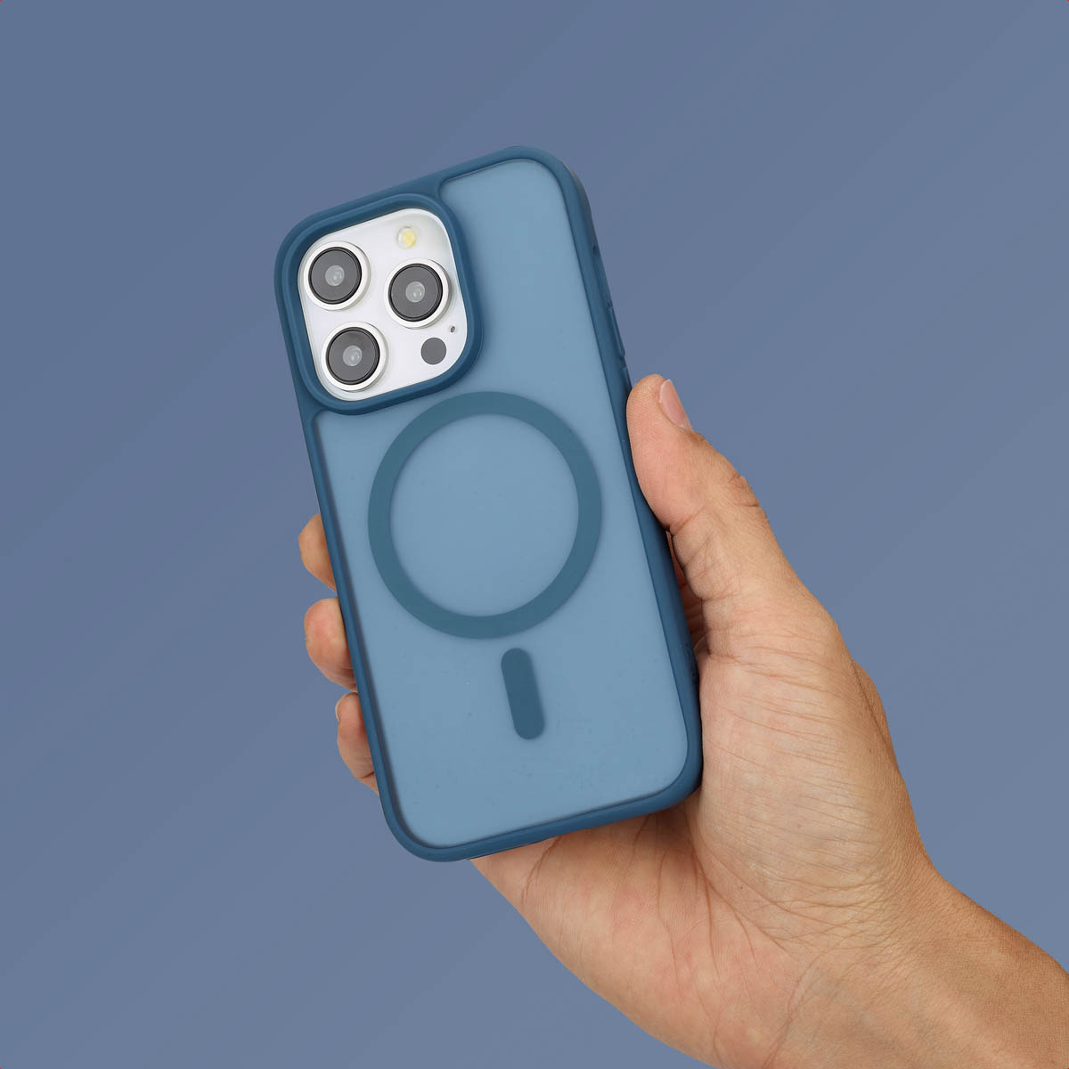 Hand die een telefoon vasthoudt met een blauwe hoes, met de MagSafe cirkel, op blauwe achtergrond.
