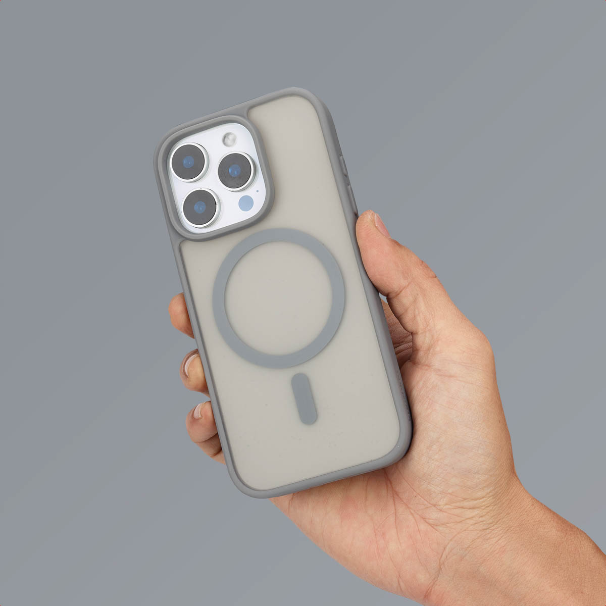 Hand die een telefoon vasthoudt met een grijze hoes, met de MagSafe cirkel, op grijze achtergrond.