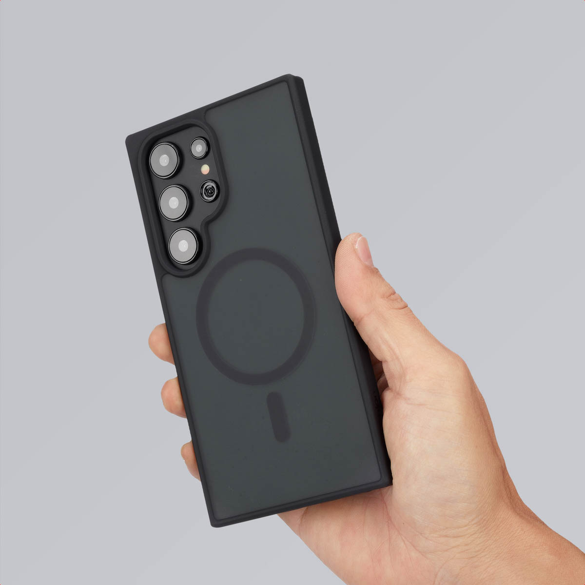 Hand die een telefoon vasthoudt met een zwarte hoes. De hoes heeft een magnetische cirkel op de achterkant.