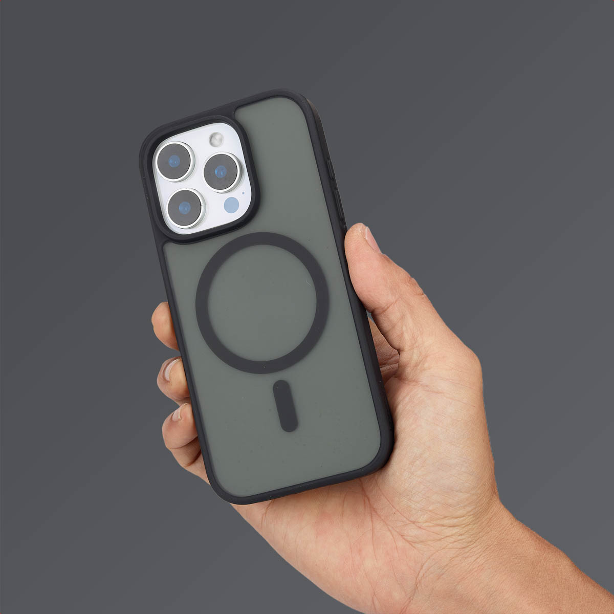 Hand houdt een donkergrijze telefoon in een hoesje vast, op een donkergrijze achtergrond. Zwarte cirkel op de achterkant.