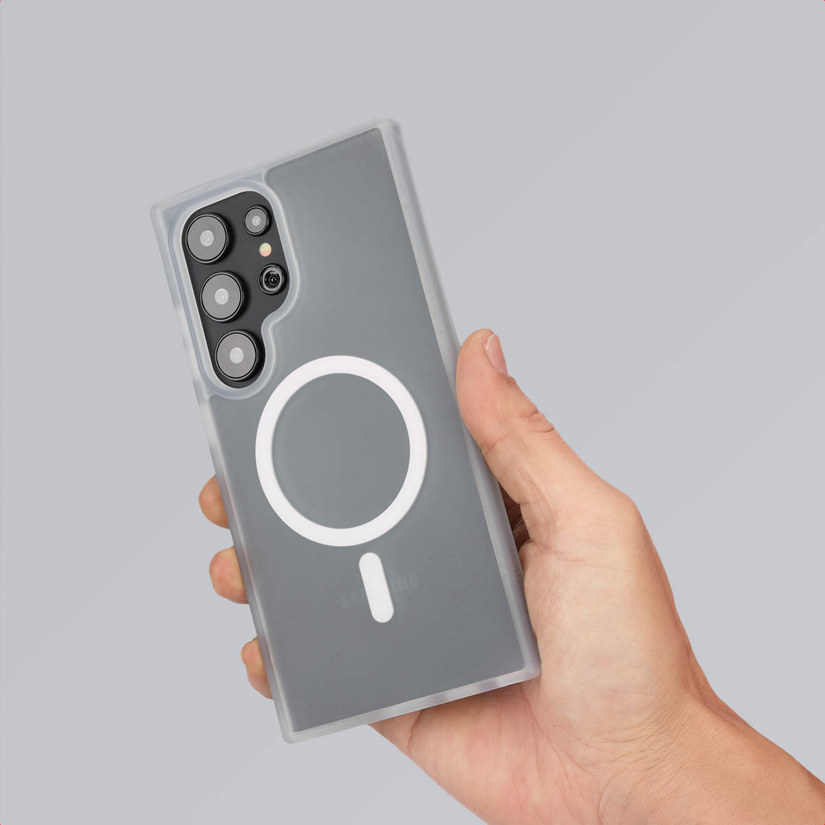 Hand die een grijs telefoonhoesje vasthoudt. MagSafe-cirkel en minteken zichtbaar.