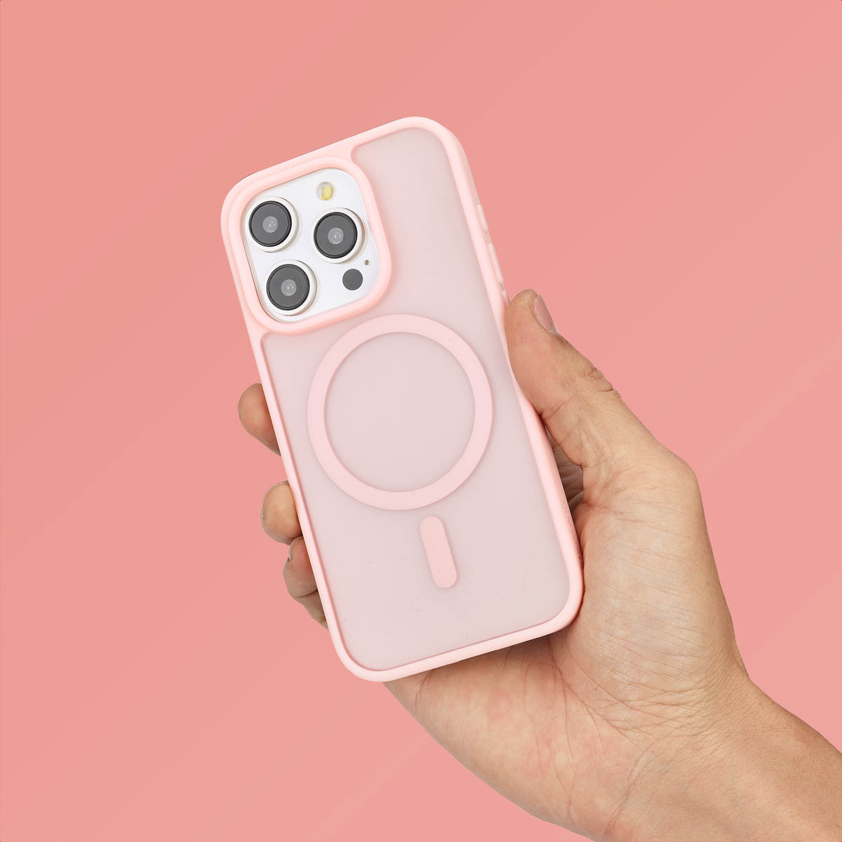 Een hand die een roze telefoonhoes vasthoudt met een MagSafe-ring. Roze achtergrond. De telefoon is niet zichtbaar.