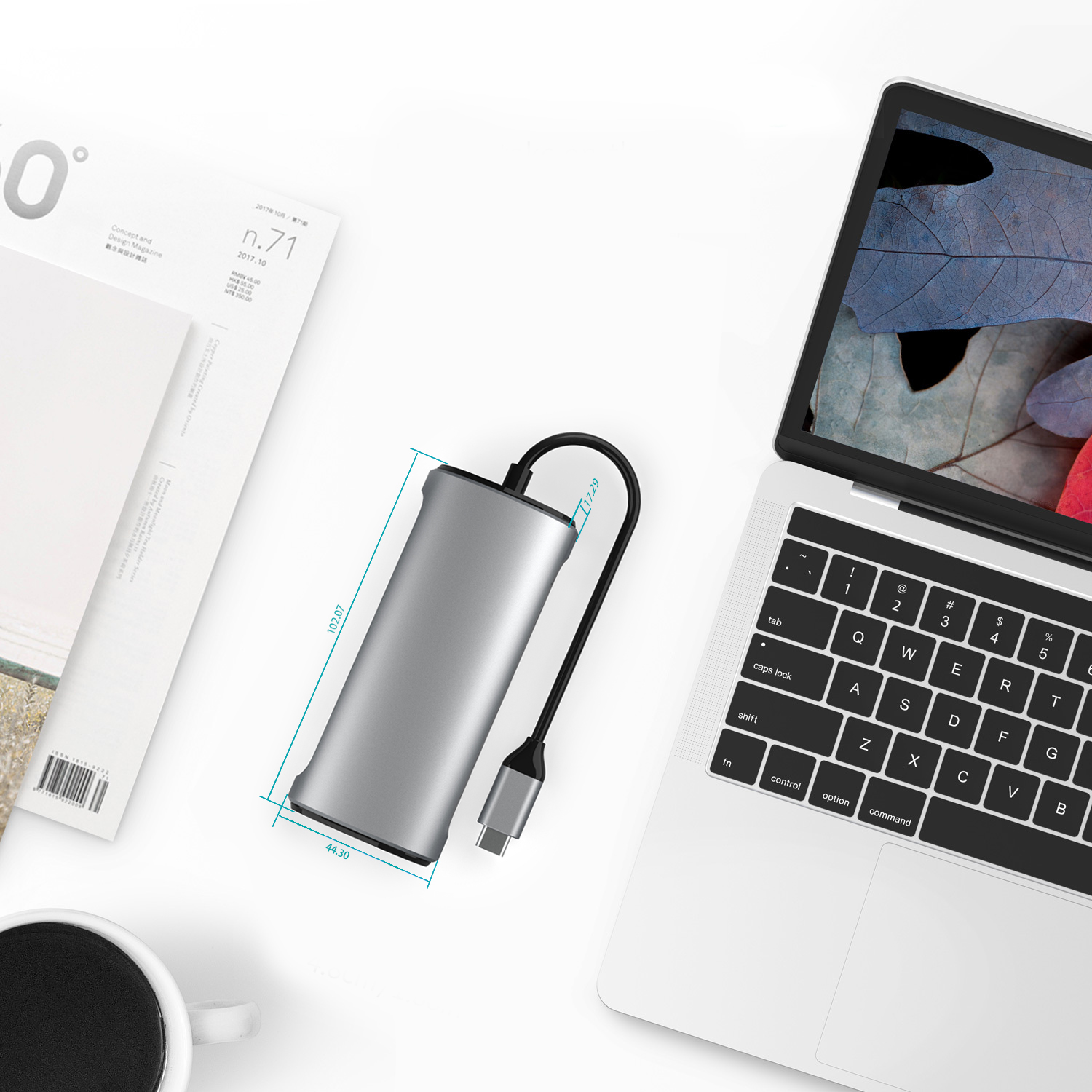 Een zilveren hub met een zwarte kabel aangesloten op een laptop en een tijdschrift.
