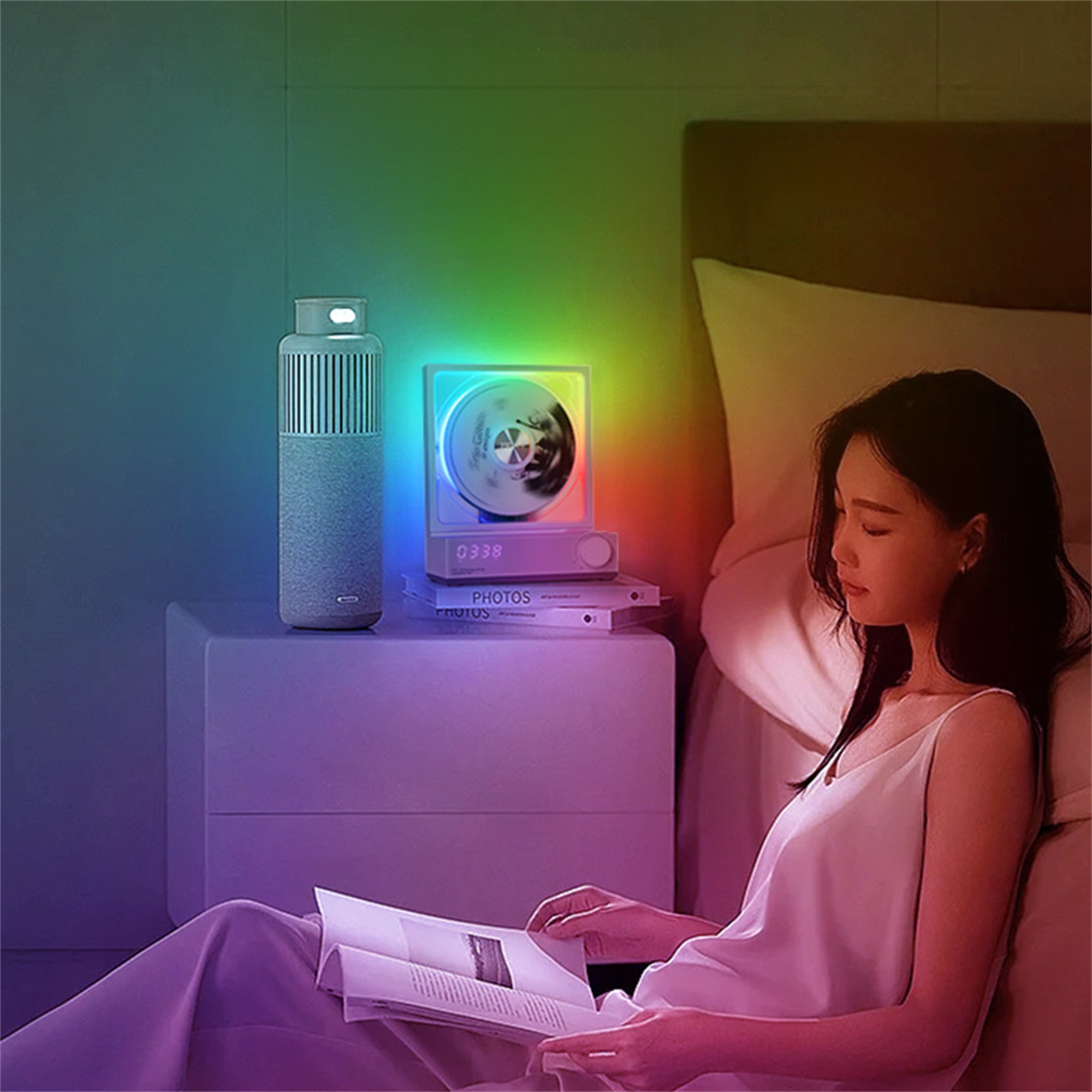 Eine Frau liest im Bett, mit einem Nachttisch, einer Lampe und einem Lautsprecher, der einen Regenbogen erzeugt.